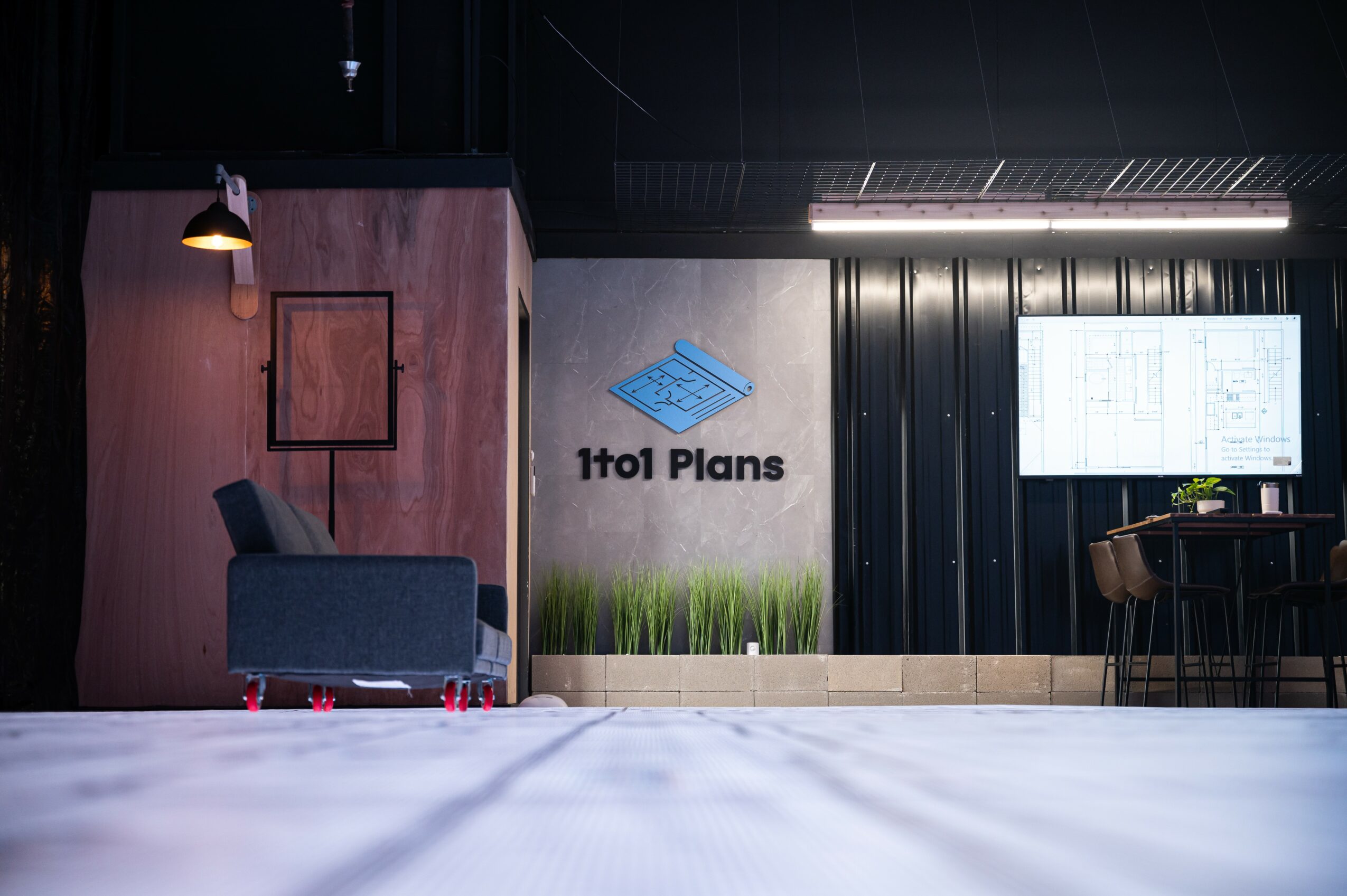 Interior office space with a sofa, wall logo, and a large screen, illuminated by ceiling lights.