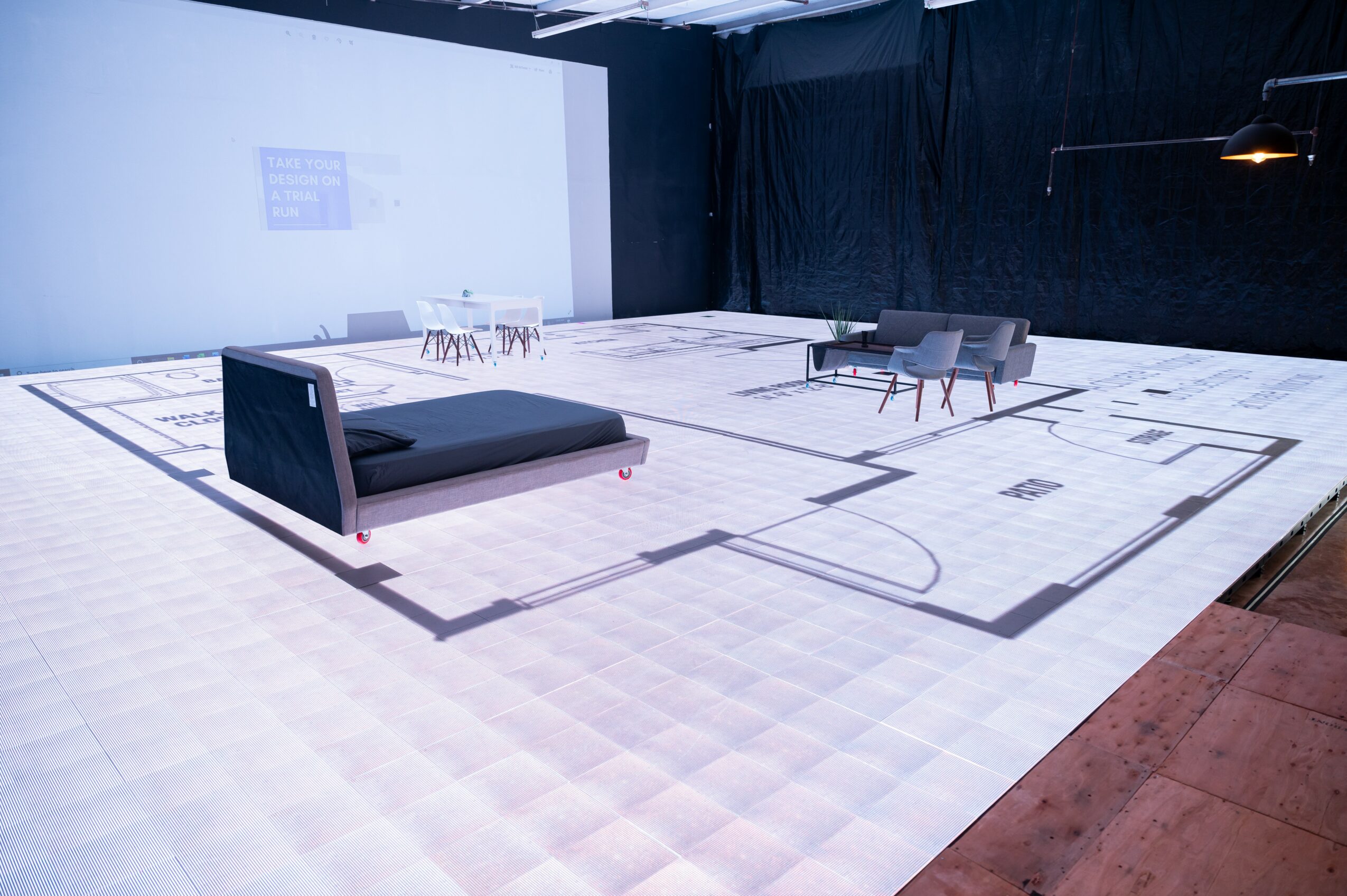 Empty indoor space with a black sofa, chairs, and a table on a white floor with black lines, walls, and curtains.