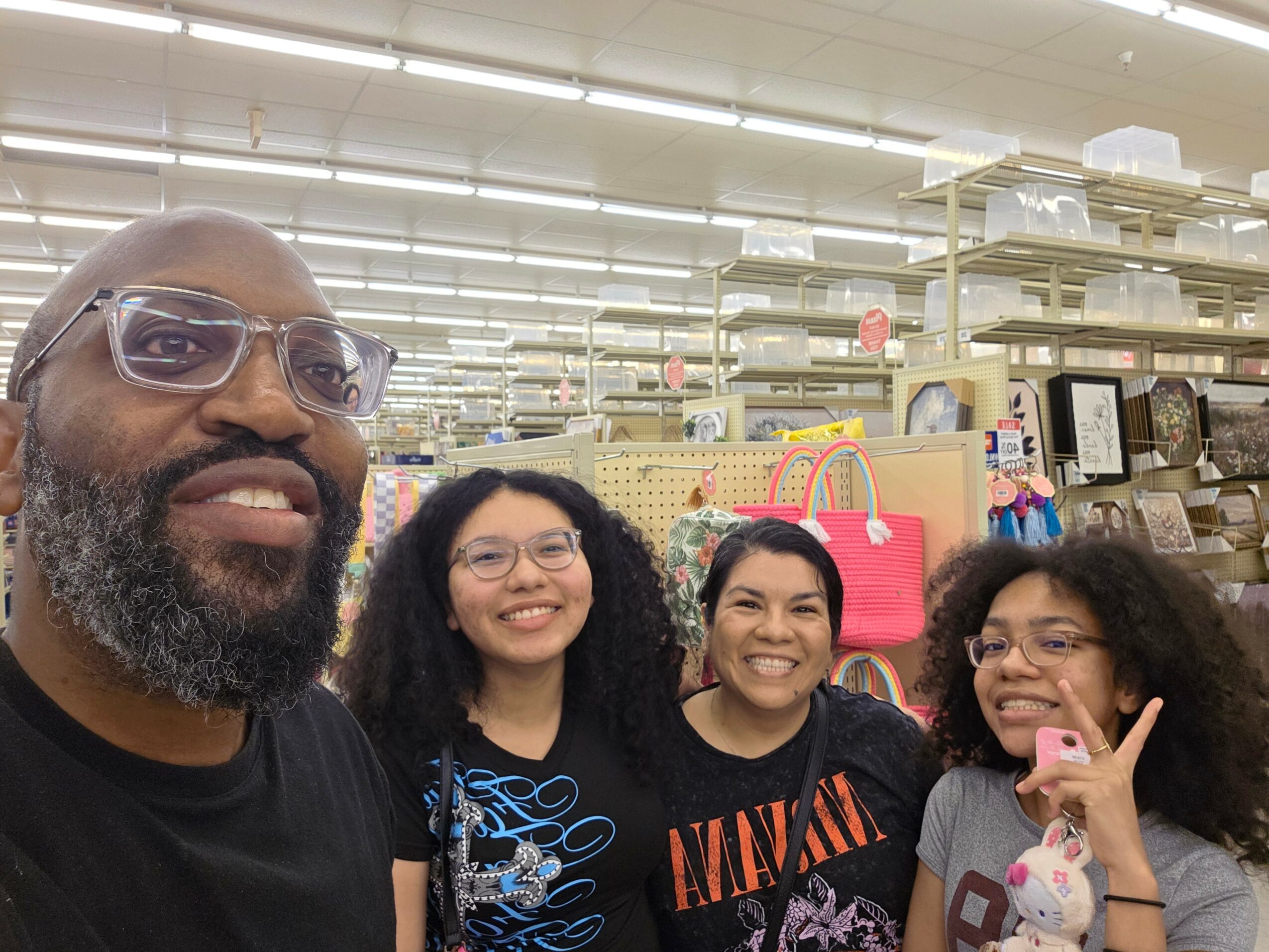 Four people smiling in a store aisle with shelves and colorful bags in the background.
