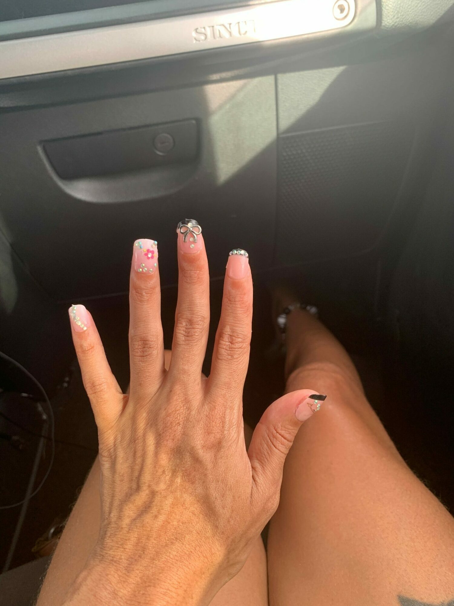 Hand resting on a person's leg, with painted nails, near a black object and a light-colored surface.