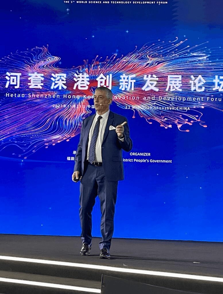 Man in suit speaking on stage with a digital background and Chinese text, at a development forum.