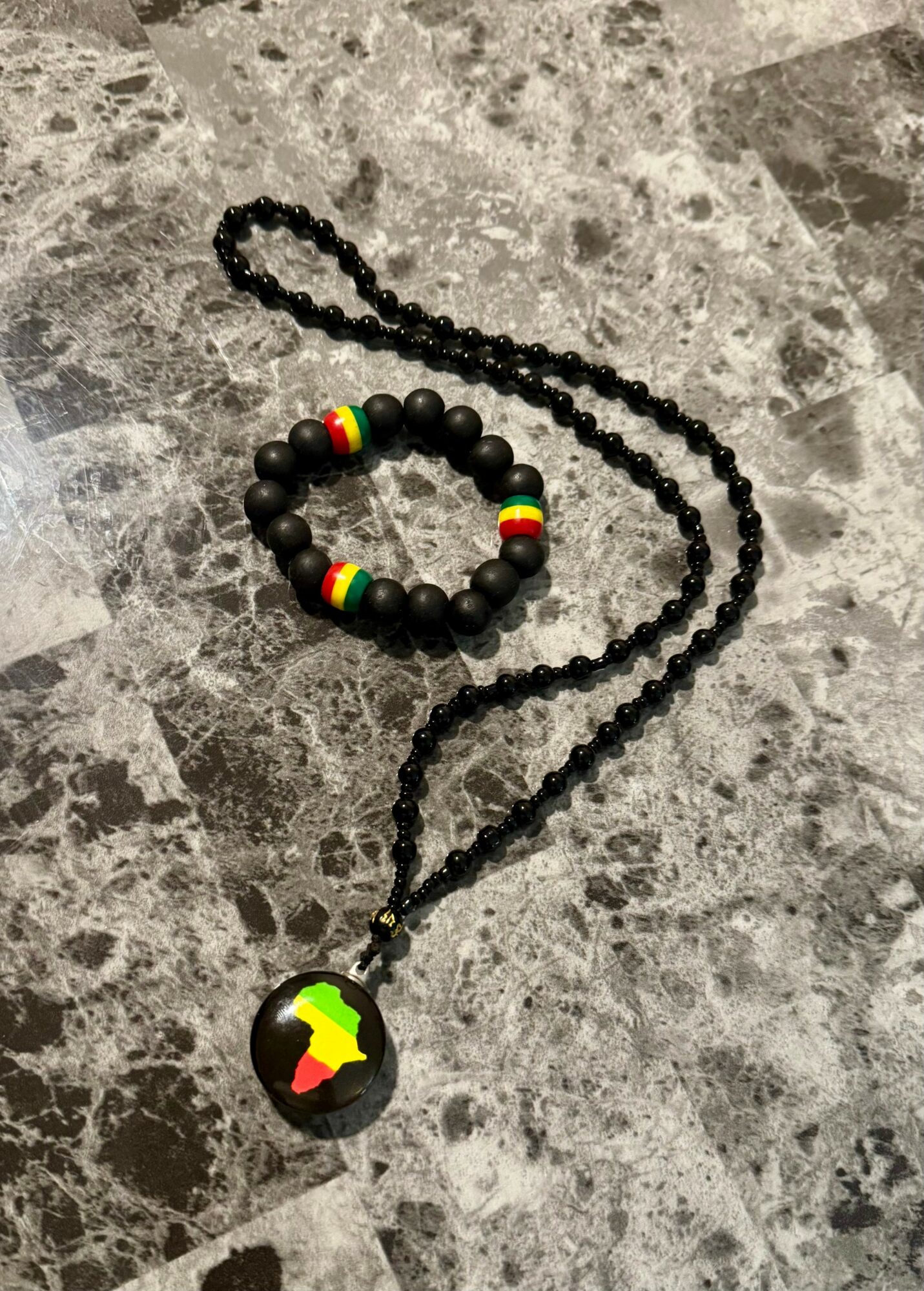Black beaded necklace with a pendant and a matching bracelet with colorful beads, placed on a gray stone surface.