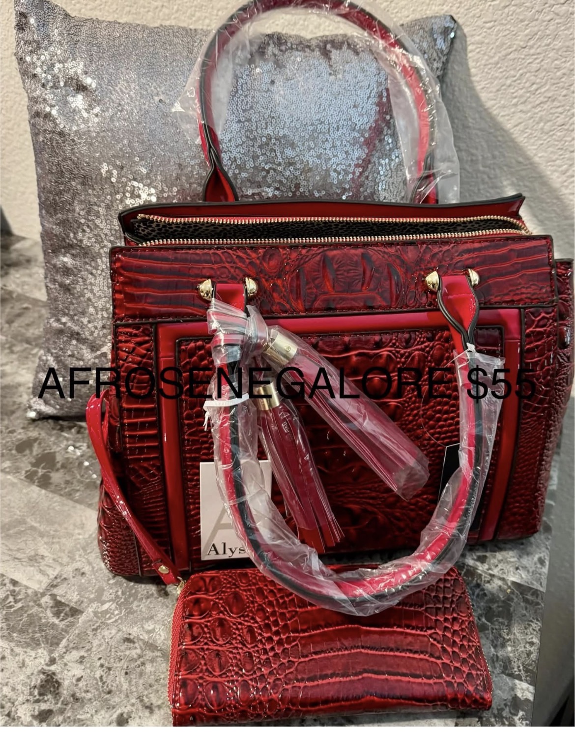 Red handbag with gold accents and a clear plastic water bottle attached, placed on a textured surface with a pillow in background.