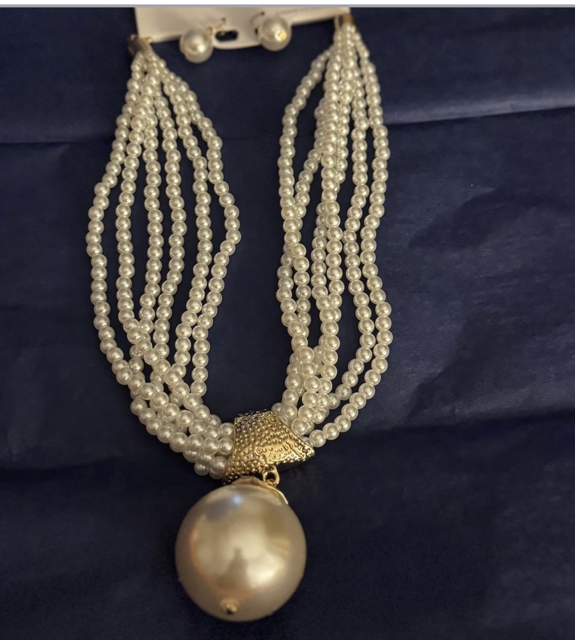Pearl necklace with multiple strands and a large pearl pendant, on dark fabric background.