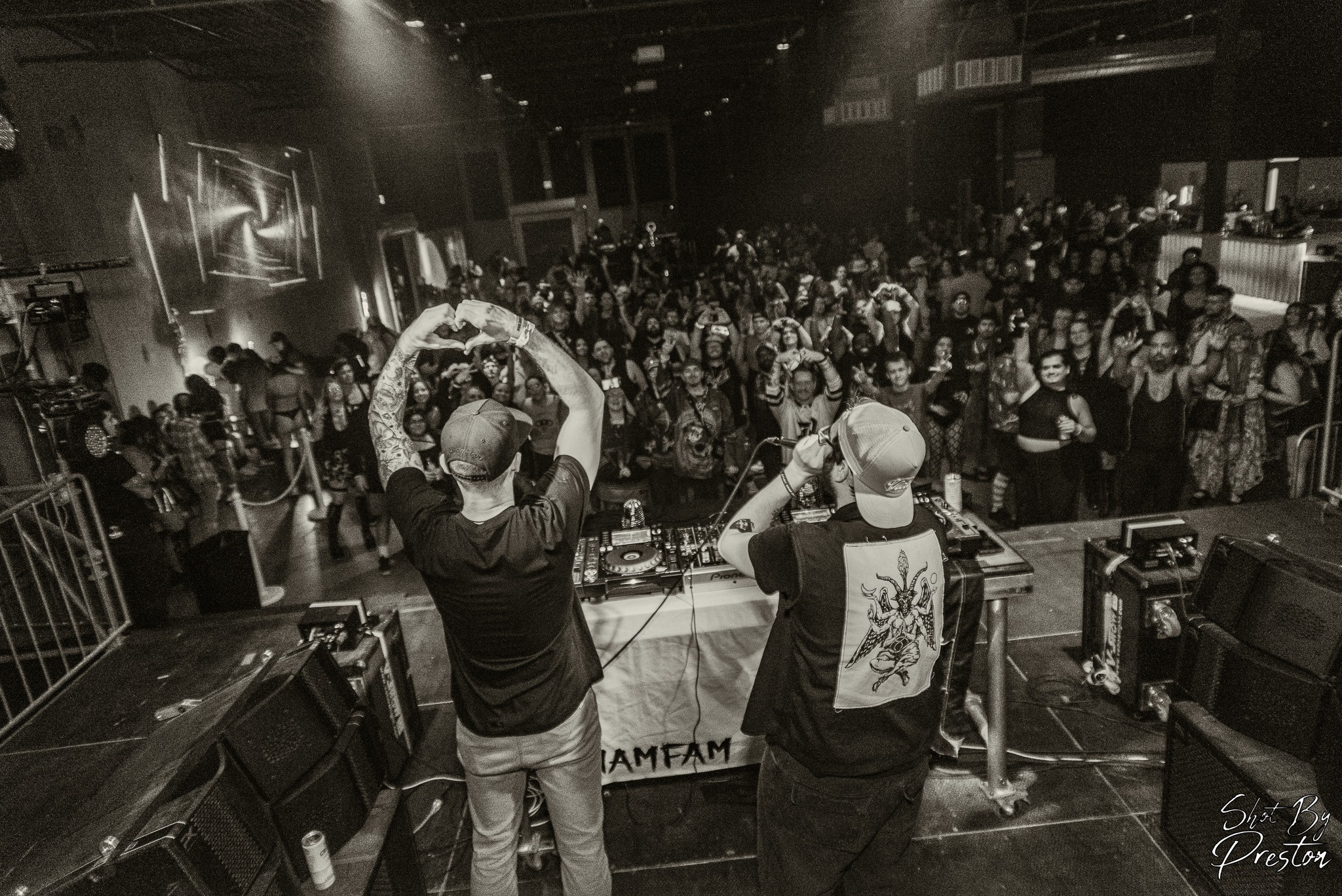 Two DJs perform on stage with a large crowd in a dark indoor venue, some people dancing and watching.