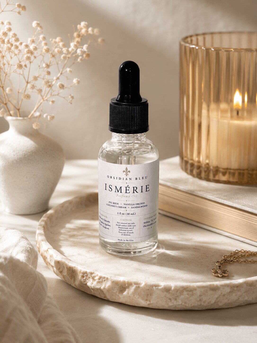 Dropper bottle labeled ISMERIE on a marble surface with a candle and decorative items nearby.