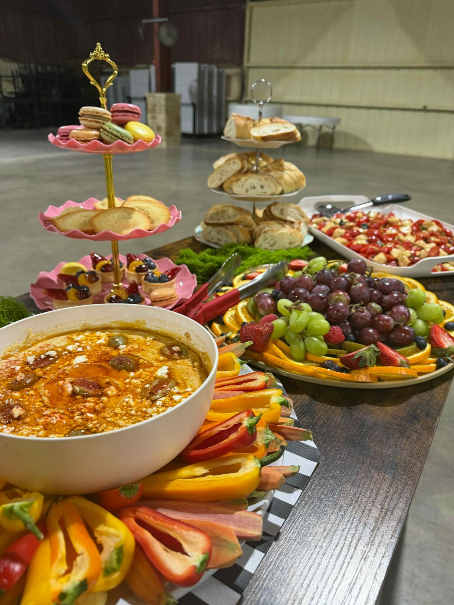 Assorted fruit platter, a bowl of baked dish, and small sandwiches on a table.