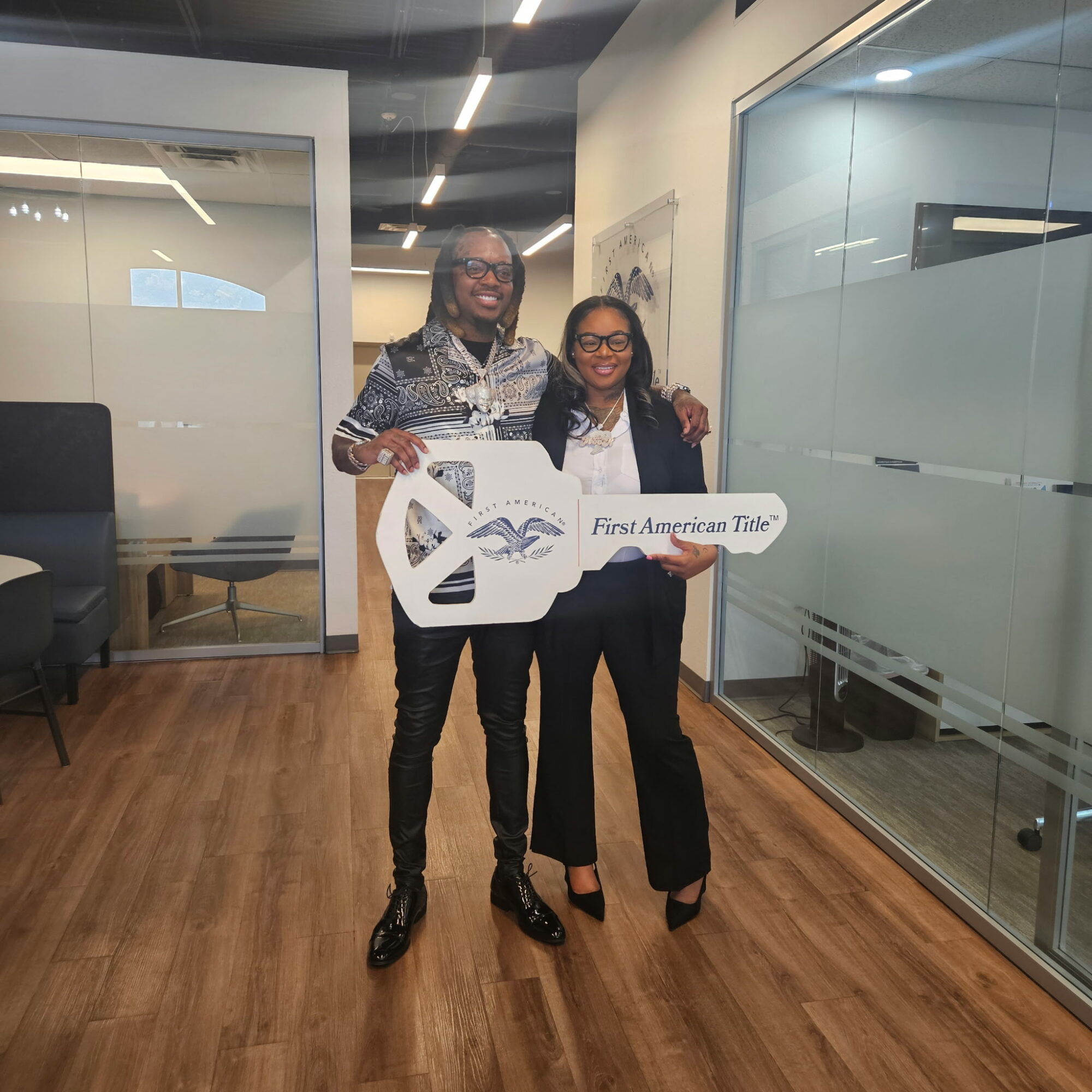 Two women stand indoors holding a large symbolic key with a logo and text, smiling at the camera.