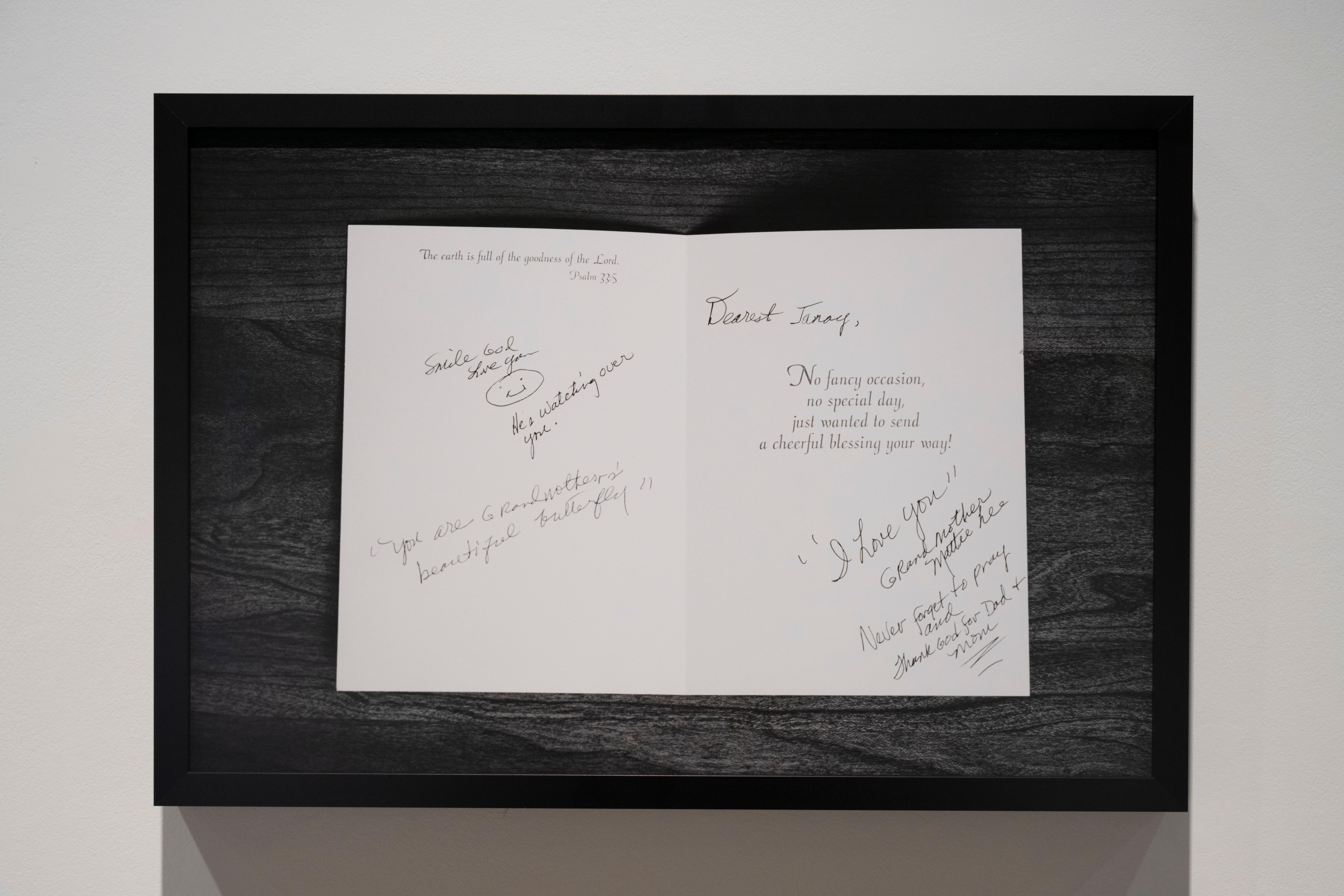 Open card with handwritten messages inside, displayed in a black frame against a white background.