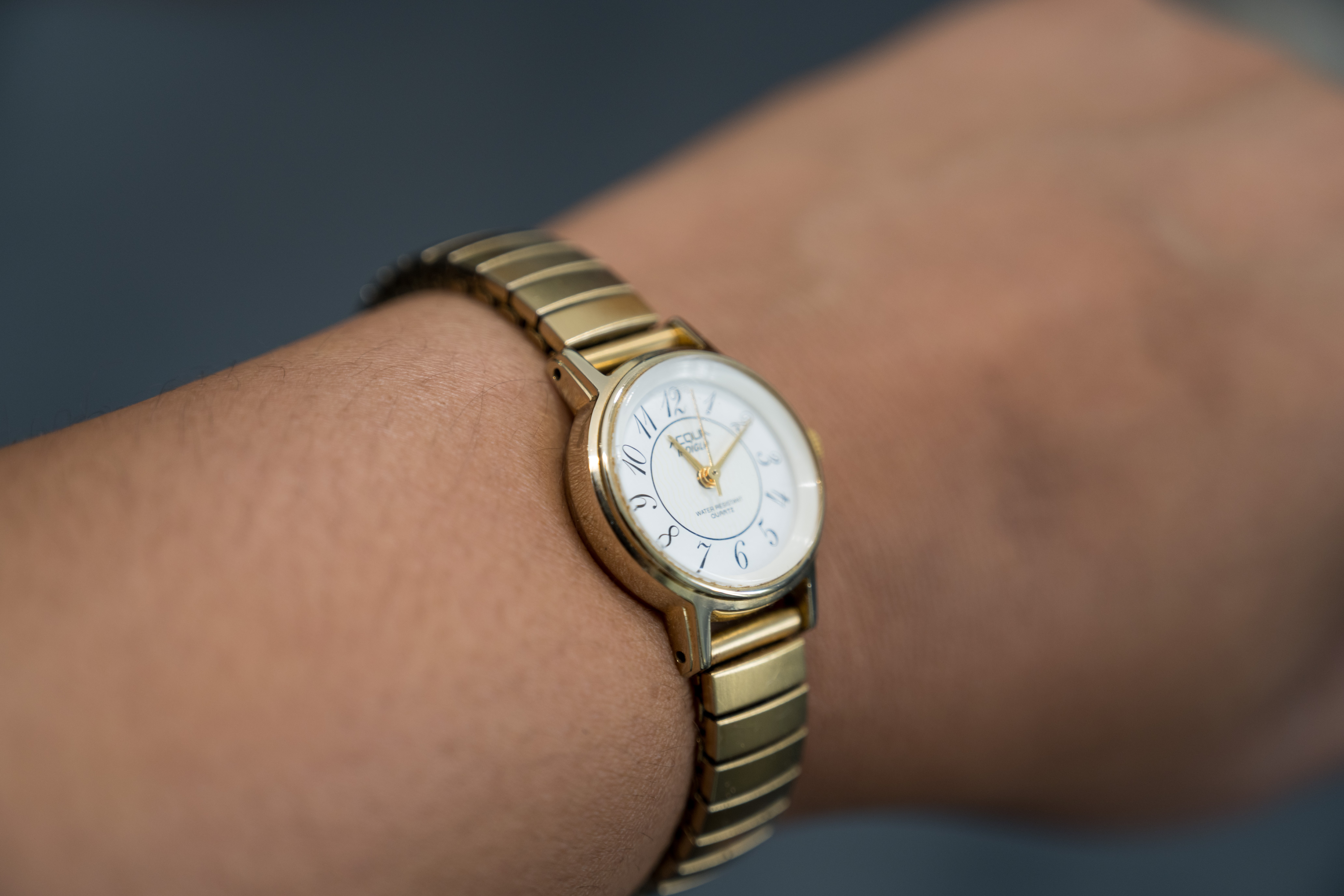Person wearing a gold wristwatch with a white face and gold details on their wrist.