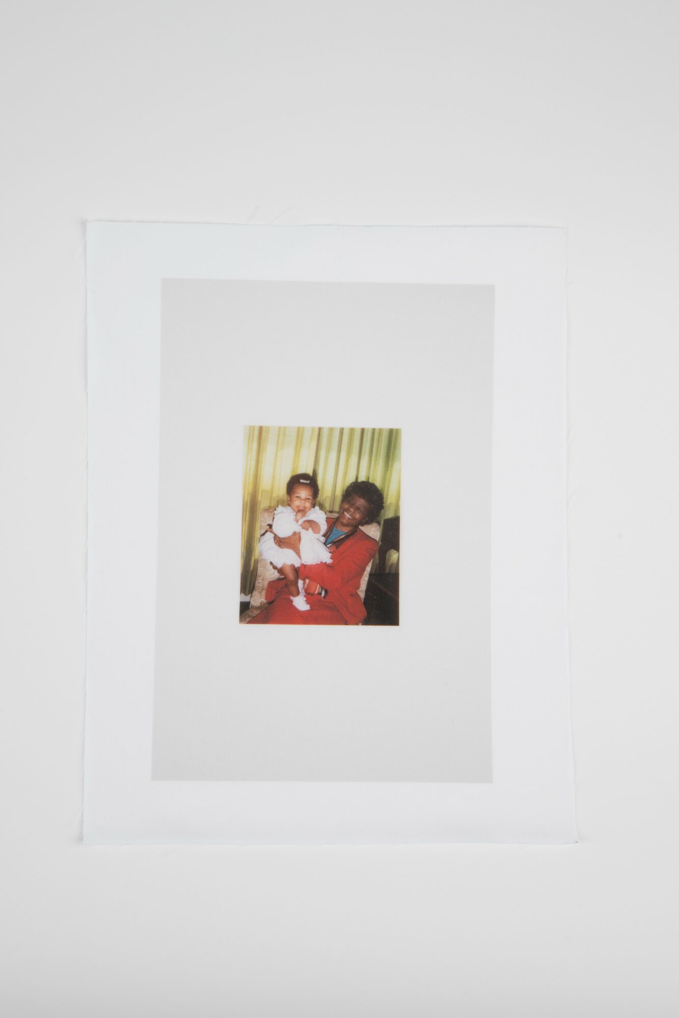 A person holding a child, both sitting in front of a curtain with vertical stripes, smiling at the camera.