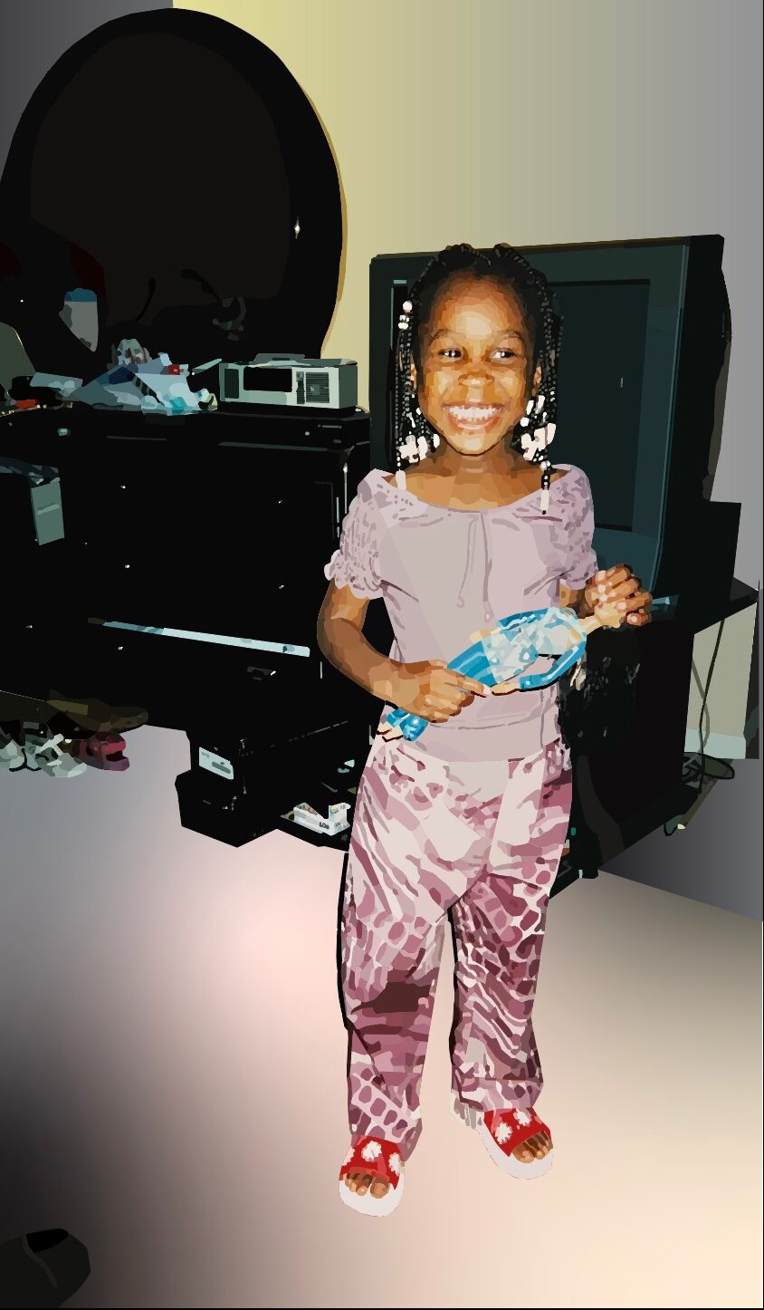 Young girl smiling, holding a toy, standing in a room with a computer and electronic devices behind her.