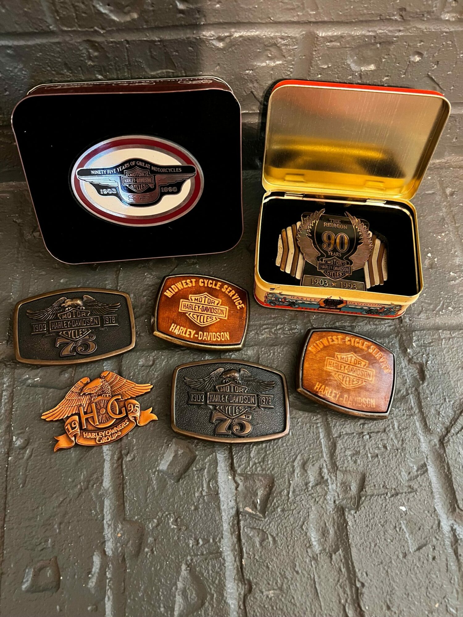 Collection of vintage metal pins and a small orange plastic figure on a gray brick surface.