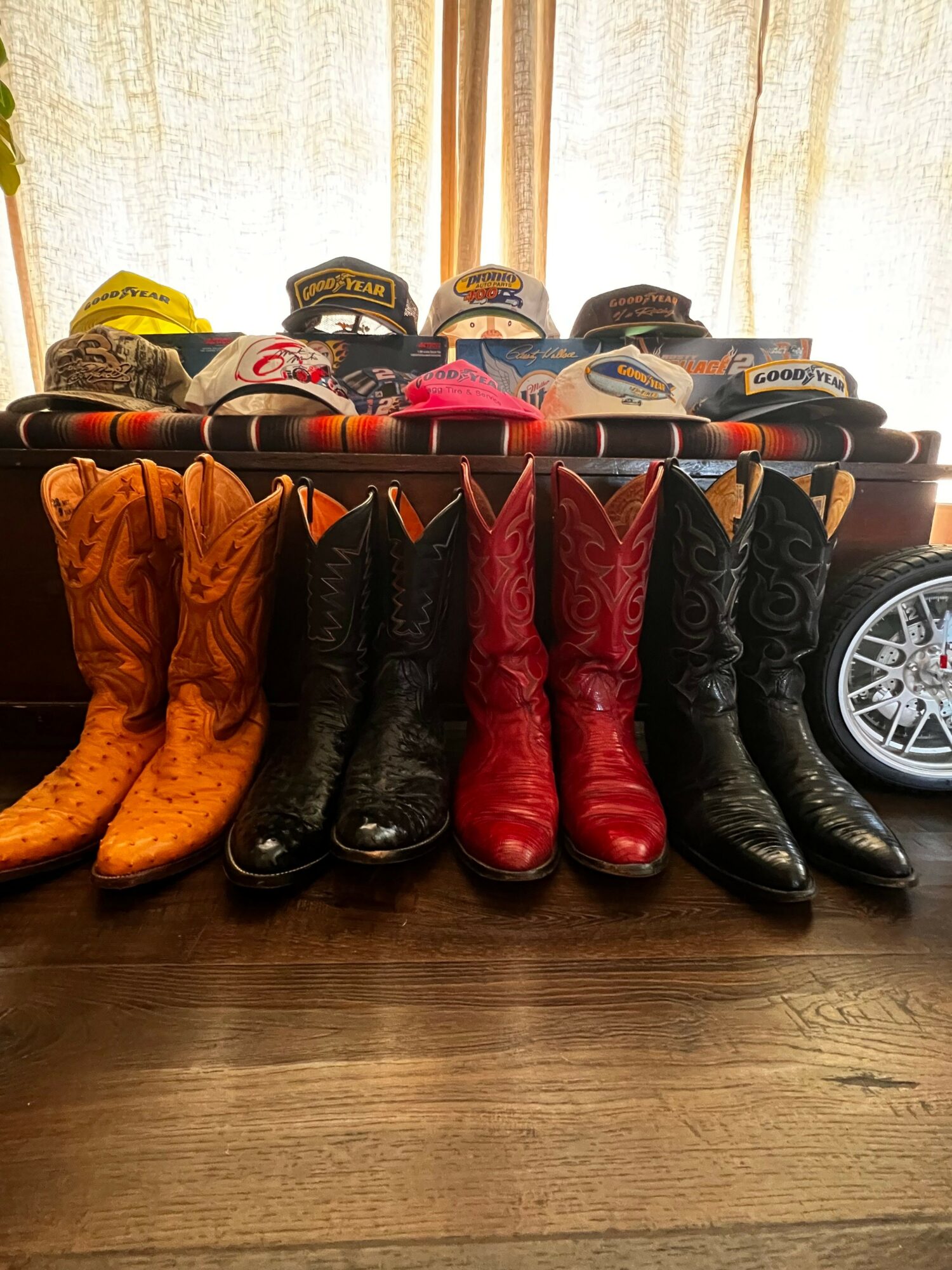 Pair of black, red, and orange cowboy boots arranged on a wooden floor with a car wheel in the background.