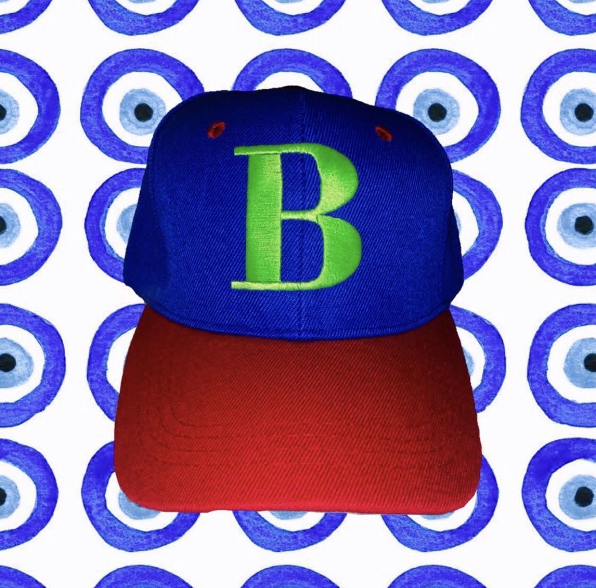 Cap with a blue crown, green letter B, and red brim, against a patterned background of blue and white circles.