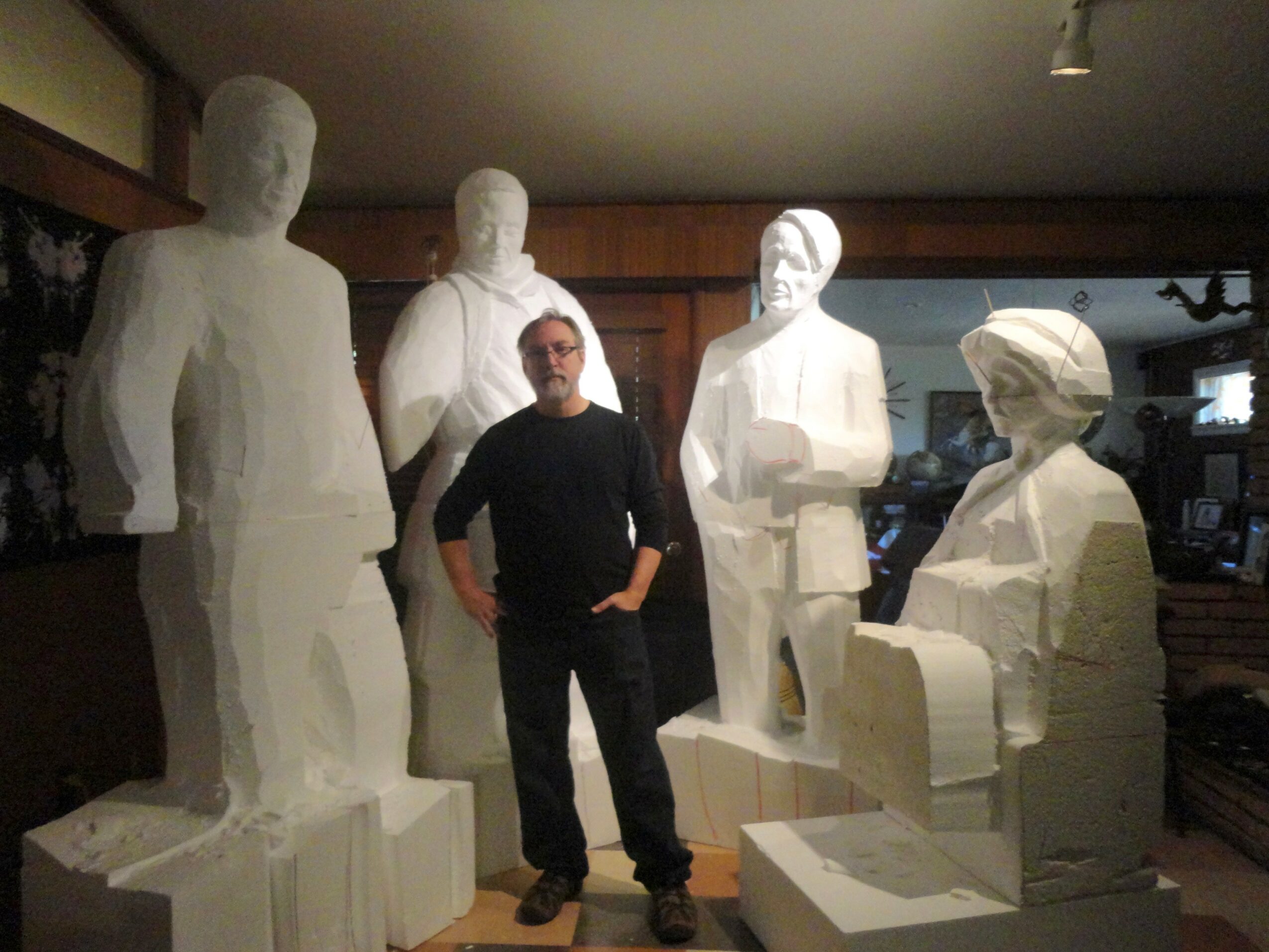 Person standing among five white statues in an indoor setting, with wooden walls and a window in the background.