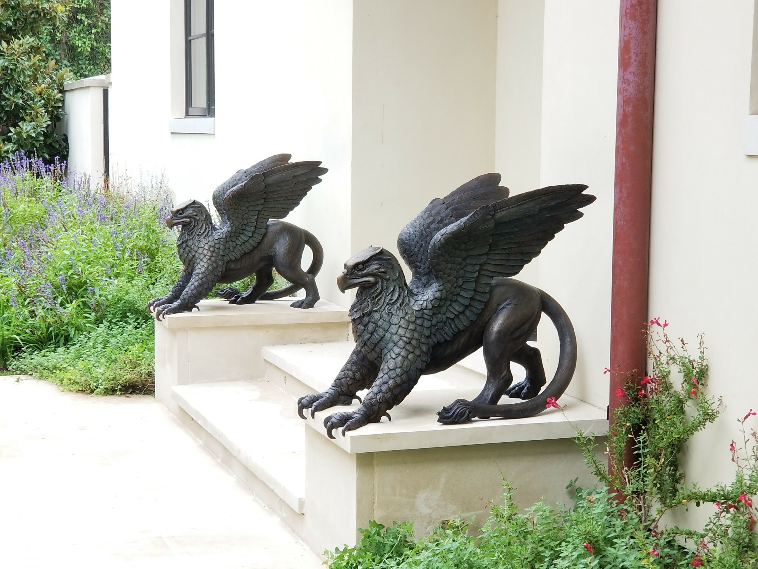 Two dragon sculptures on ledges outside a building, surrounded by greenery and plants.