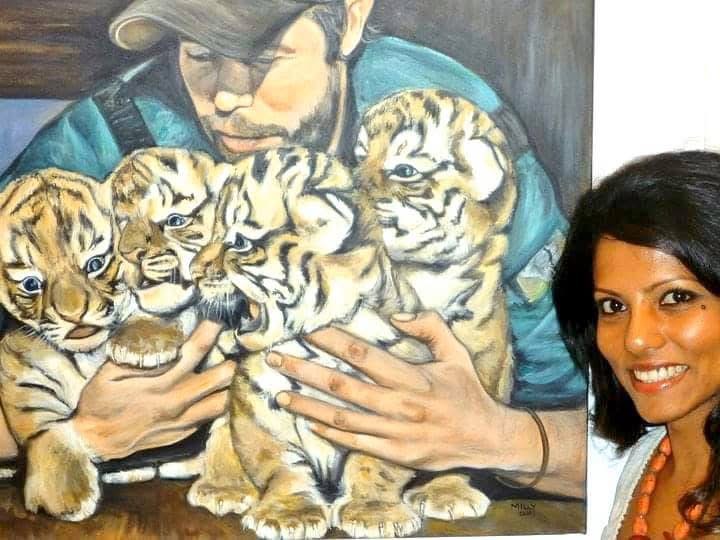 A woman holding four tiger cubs with another woman smiling nearby, in a colorful setting.