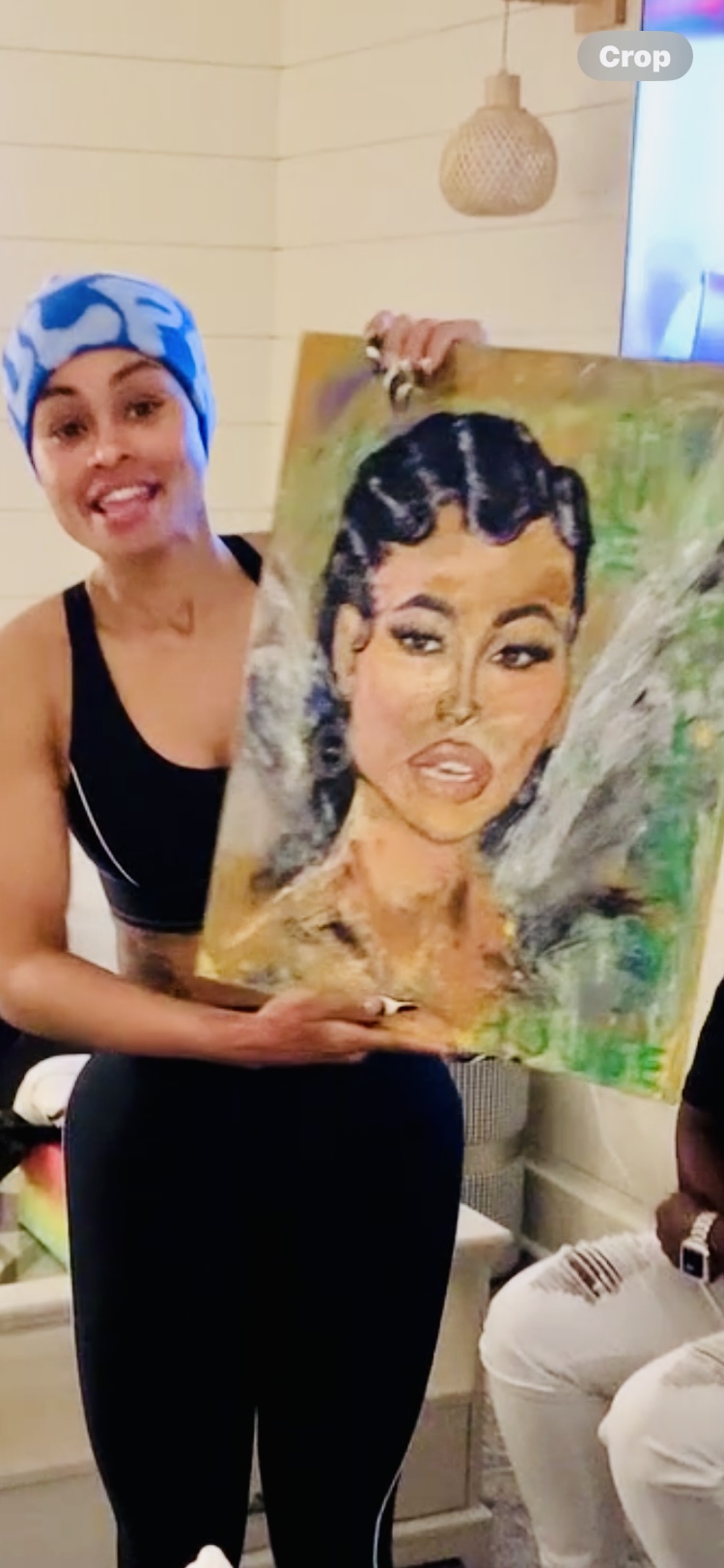 Woman smiling holding a colorful portrait painting of herself indoors.