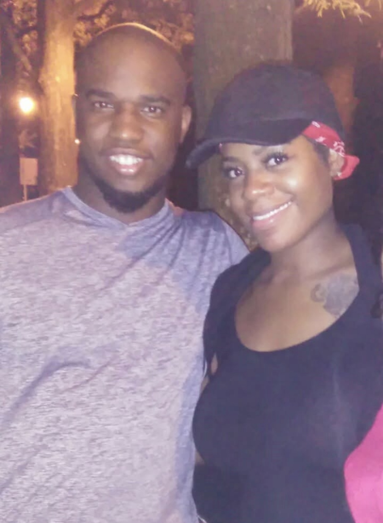 A man and woman smiling outdoors at night, with trees in the background.