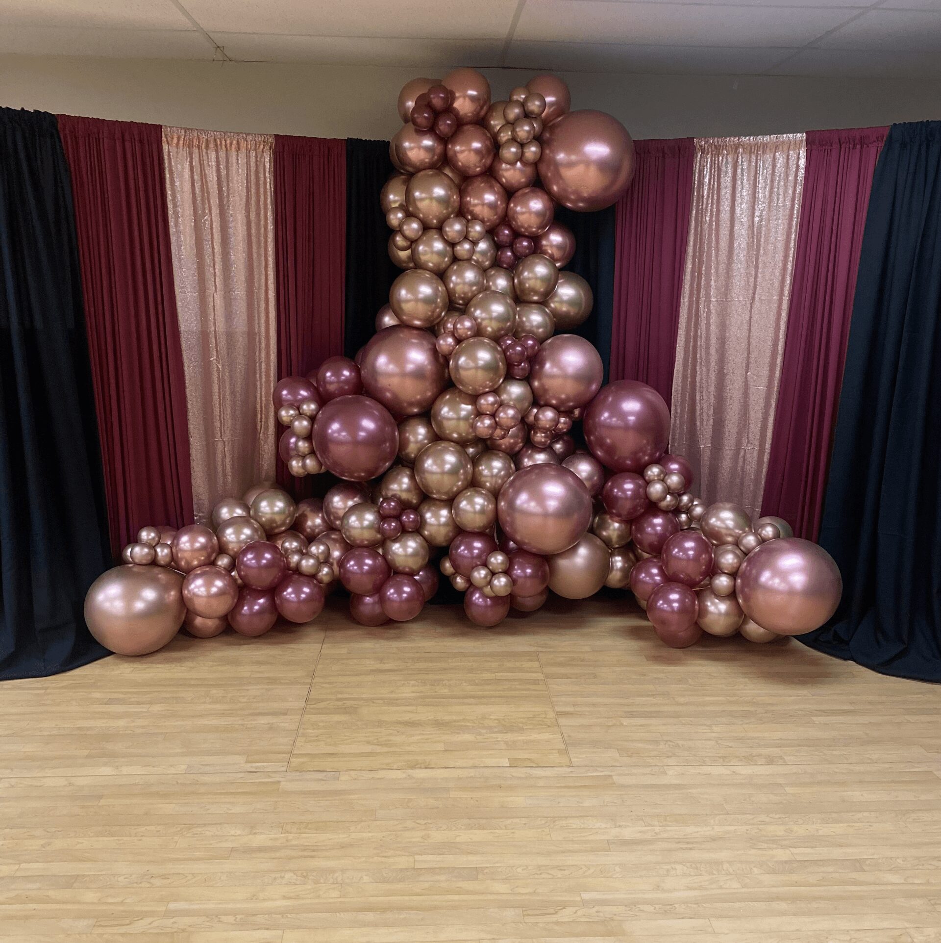Decorative arrangement of pink, gold, and bronze balloons in front of curtains with pink, cream, and dark blue panels.
