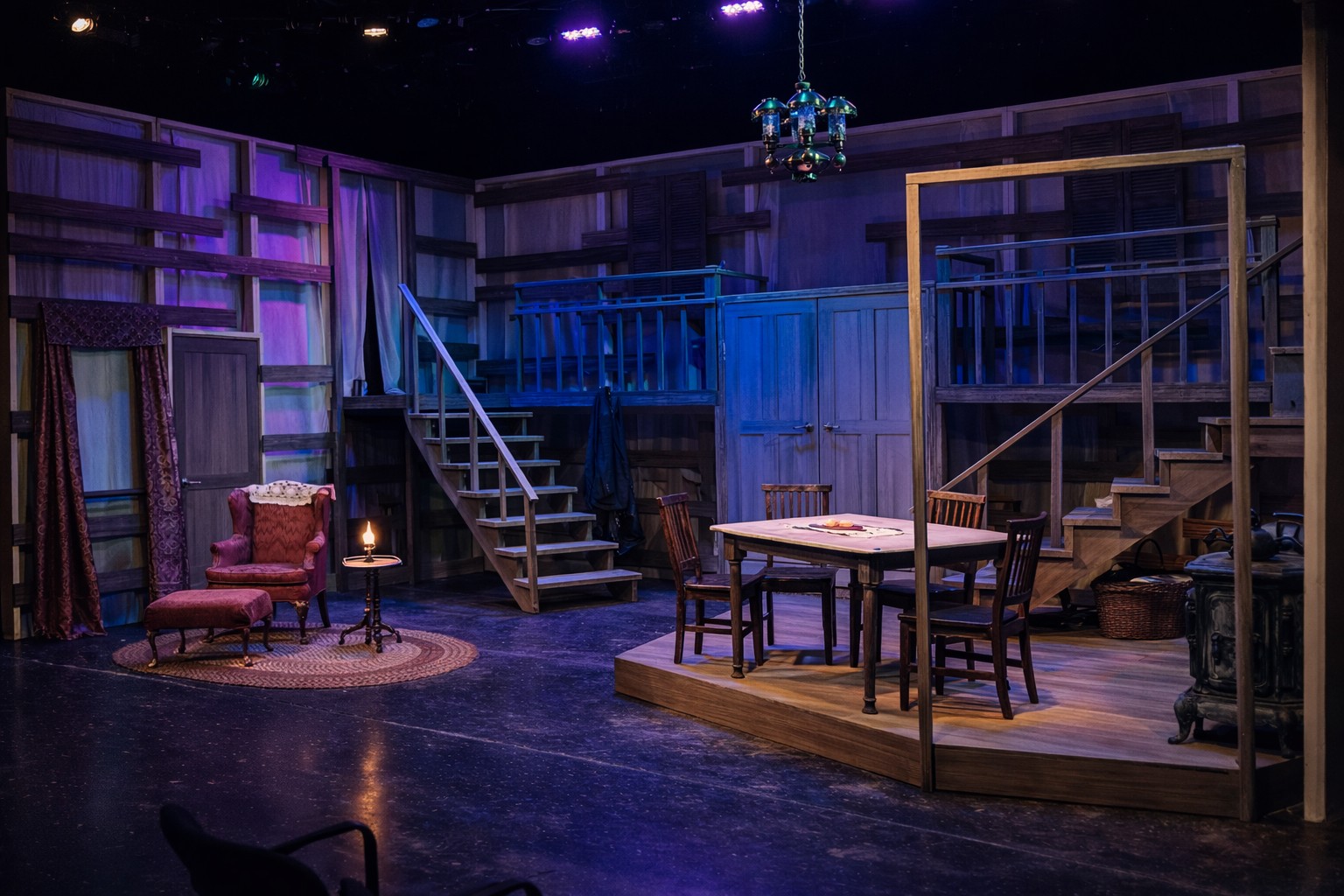 Stage set with stairs, table, chairs, and vintage furniture, illuminated by purple and blue lighting, resembling a cozy interior scene.