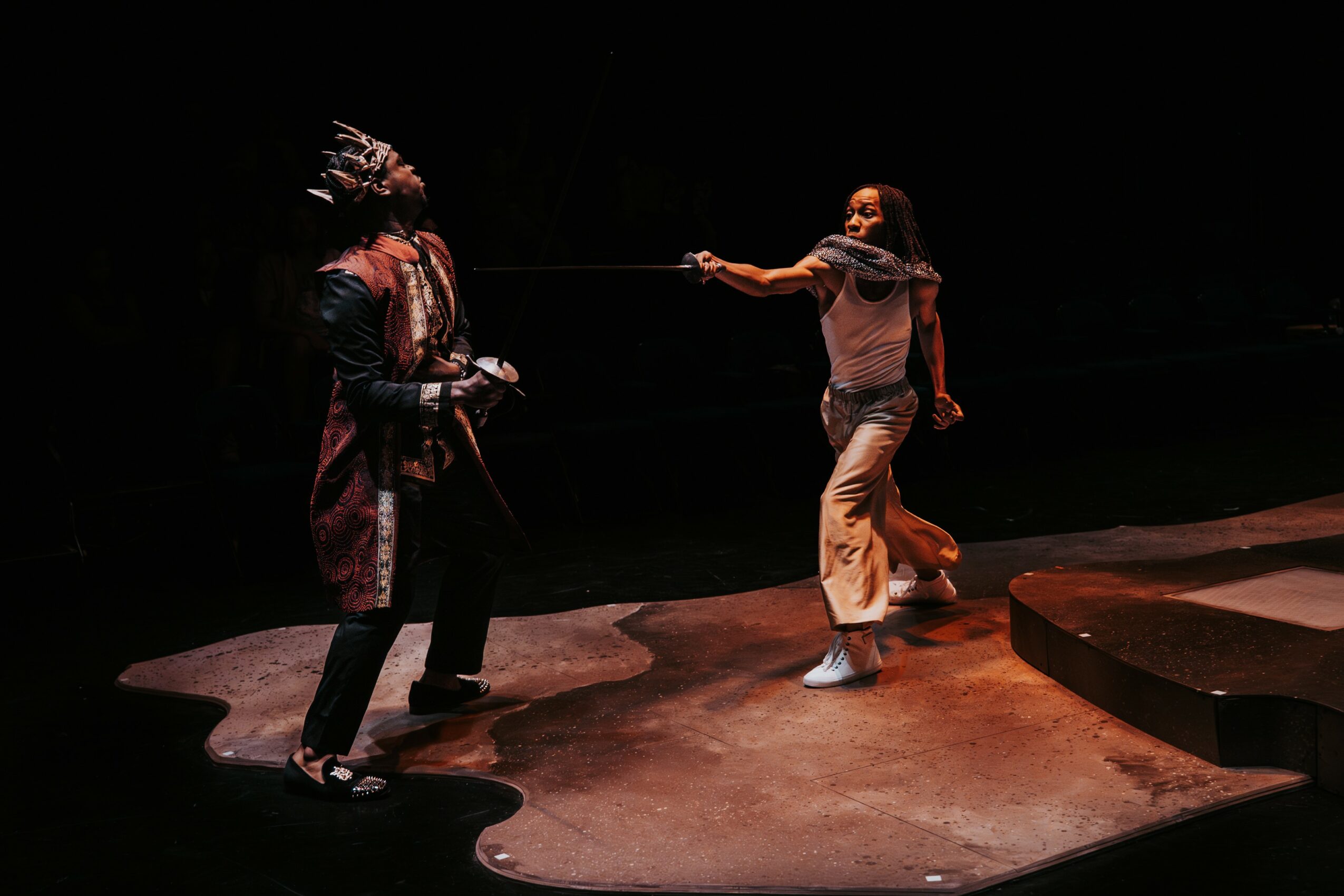 Two people engaged in a theatrical performance on a dark stage, one pulling a rope and the other holding it, with dramatic lighting.