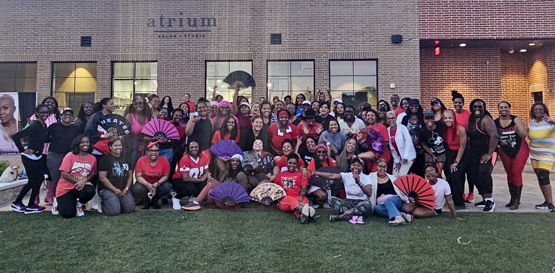 Large group of people outdoors in front of a building, some holding umbrellas, posing for a photo.