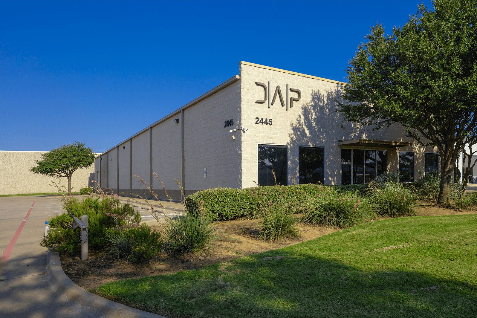 Commercial building with a sign, surrounded by trees and bushes, under a clear blue sky.