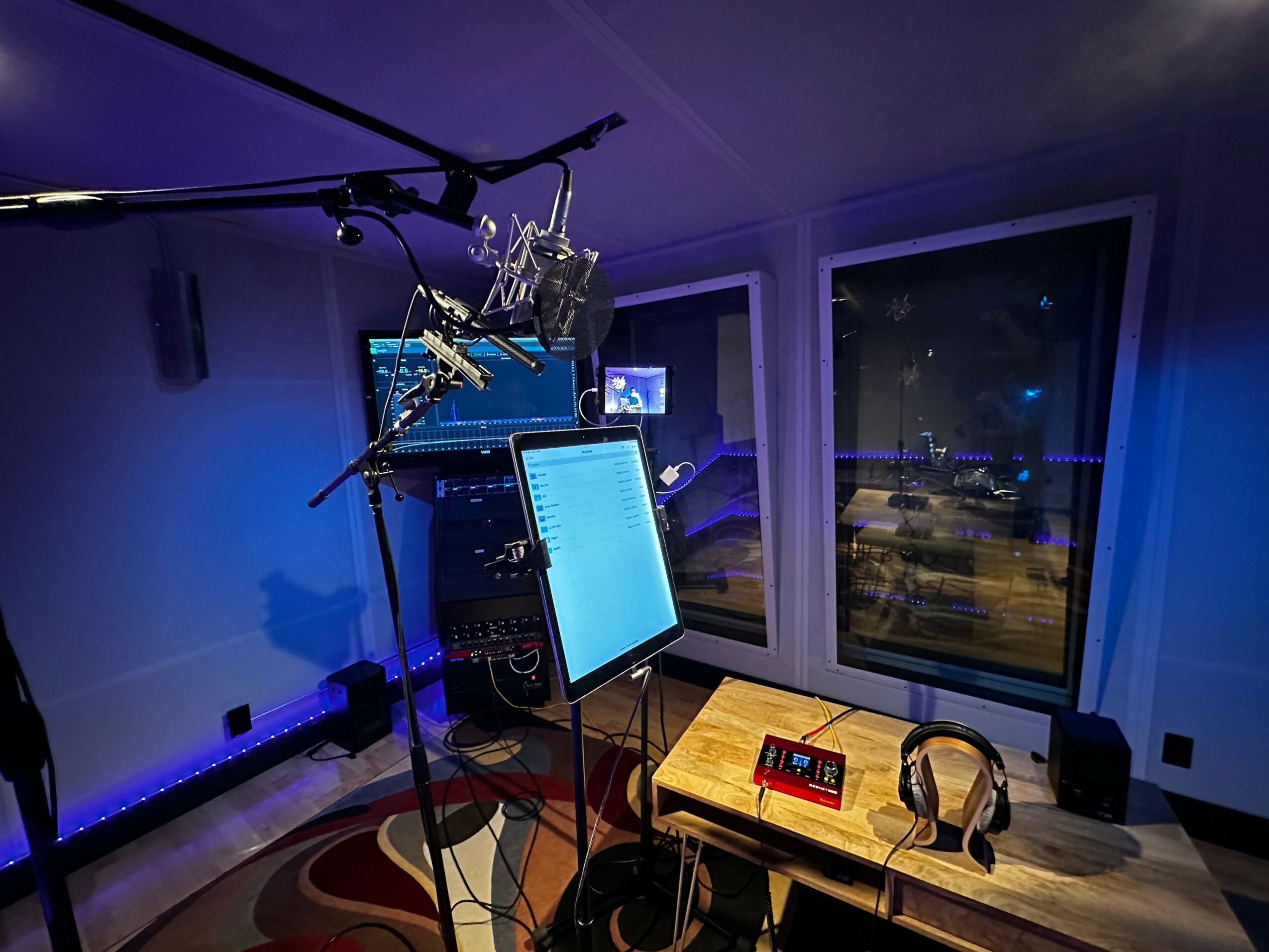 Recording studio with computer monitor, microphone, headphones, and window showing city lights at night.