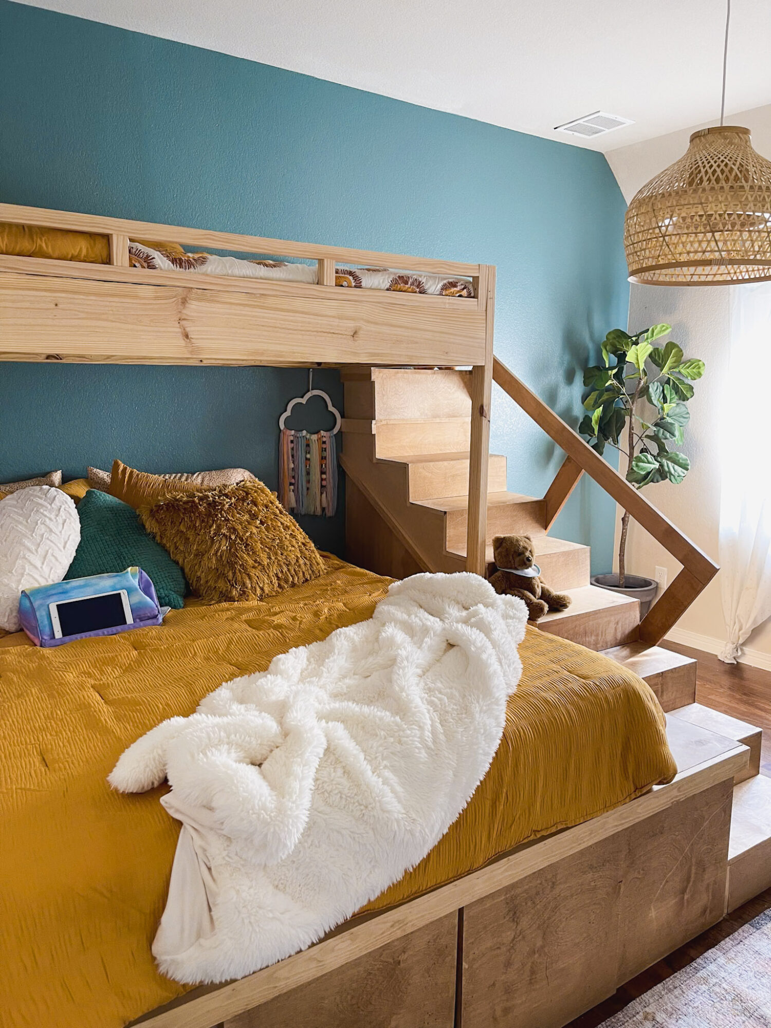 Bedroom with a wooden loft bed, teal wall, and a bed with mustard bedding and a white blanket, next to a plant.