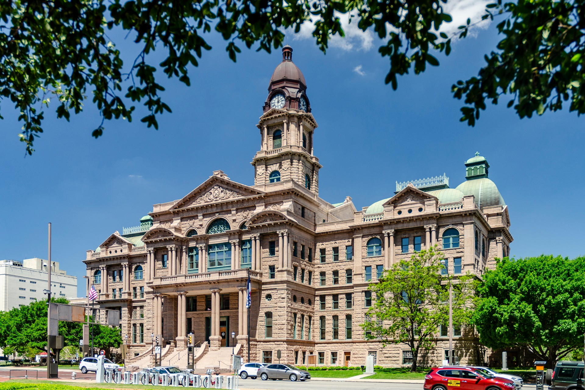 Historic government building with a central clock tower, surrounded by trees and a clear blue sky.