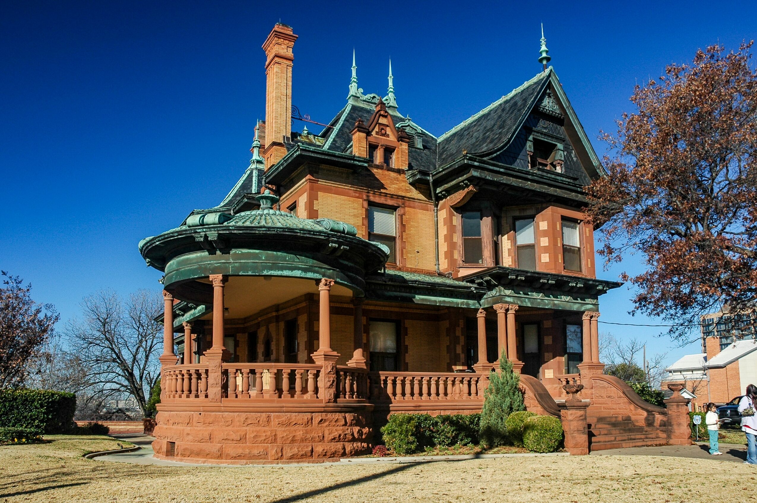 Victorian-style house with a turret, porch, and stairs, surrounded by trees and a clear blue sky.