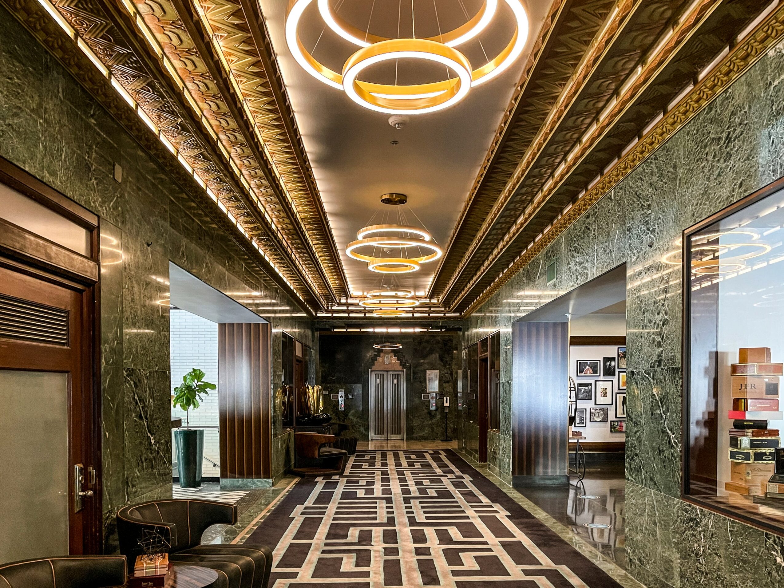 Elegant corridor with green marble walls, decorative gold accents, modern circular ceiling lights, and patterned floor tiles.