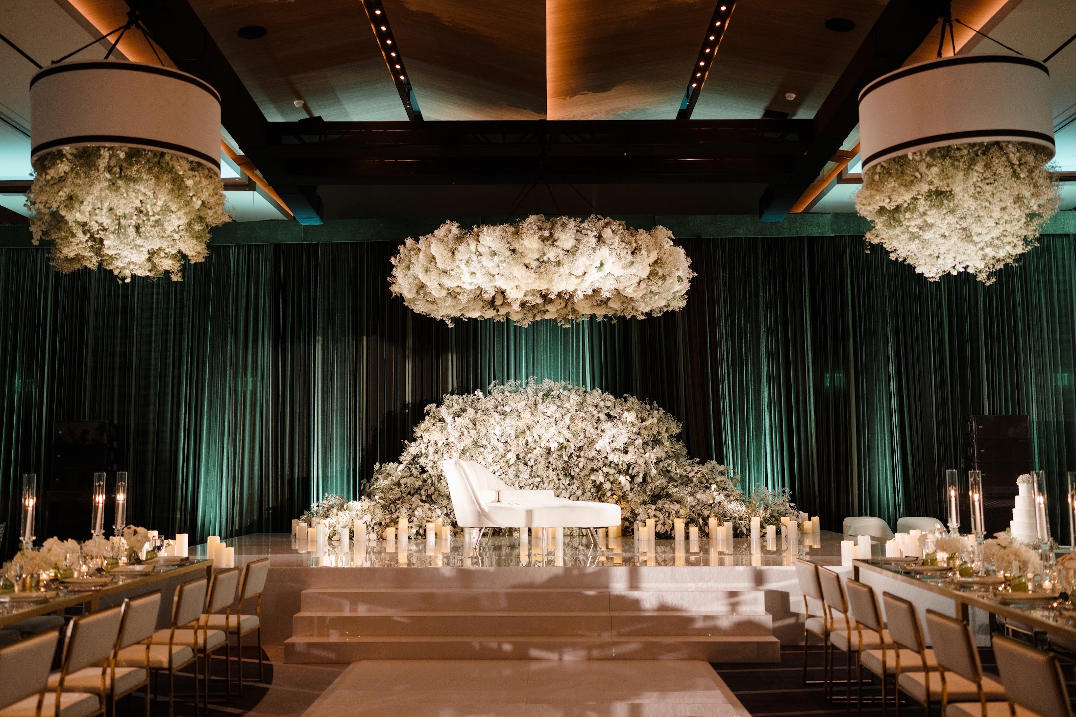 Elegant event space with floral arrangements, a white grand piano, and draped curtains, decorated with hanging floral chandeliers.