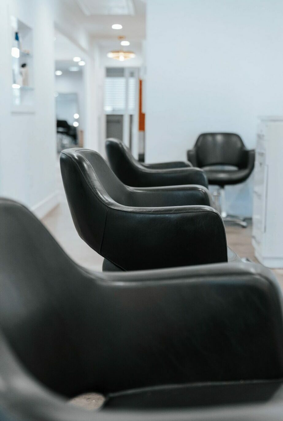 Empty salon chairs in a modern, bright hair salon with white walls and mirrors.
