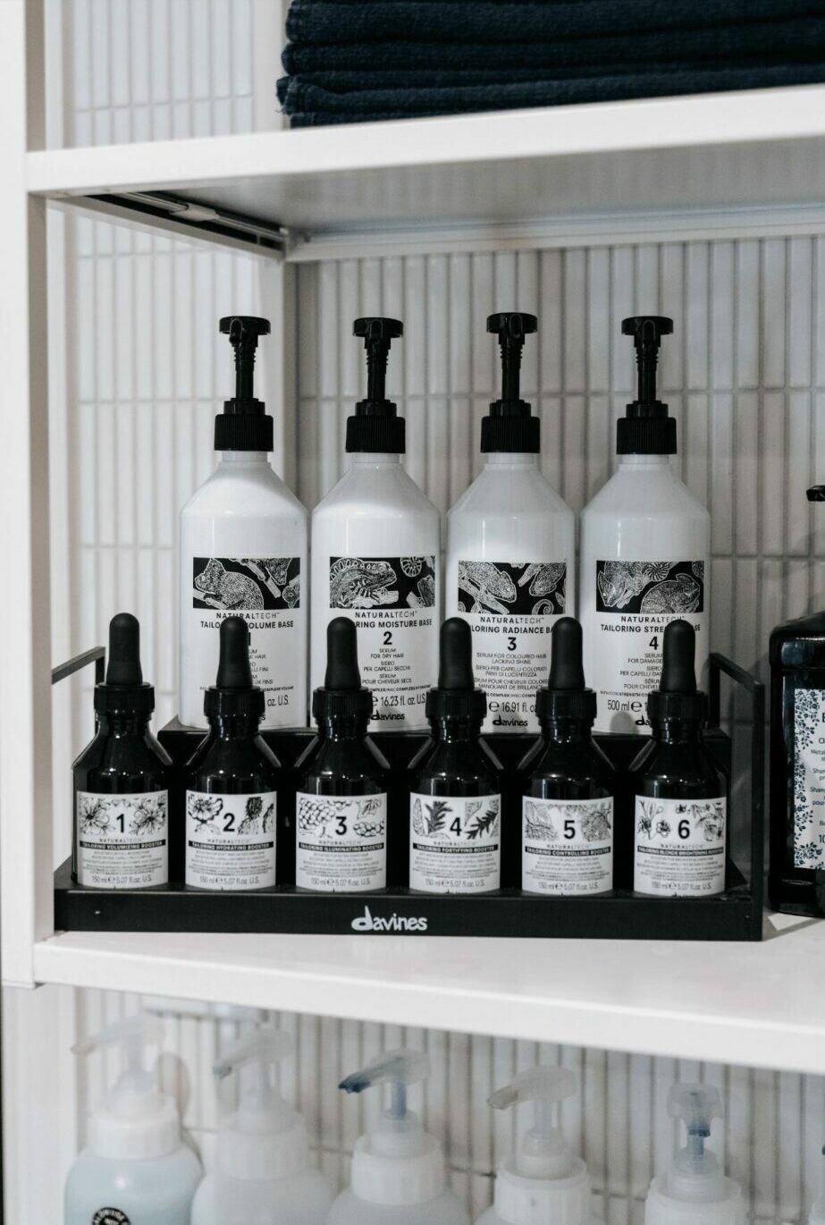 Shelf with white bottles and black dropper caps, organized on a wire rack, with folded black towels above.