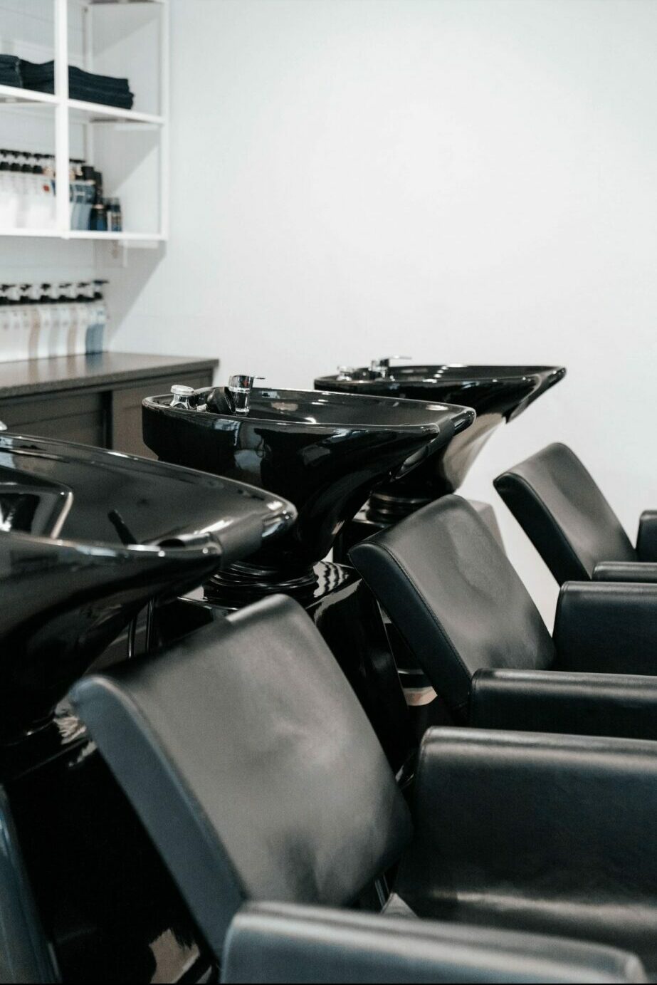Salon chairs with hair washing stations and shelves in a modern hair salon, white wall background.