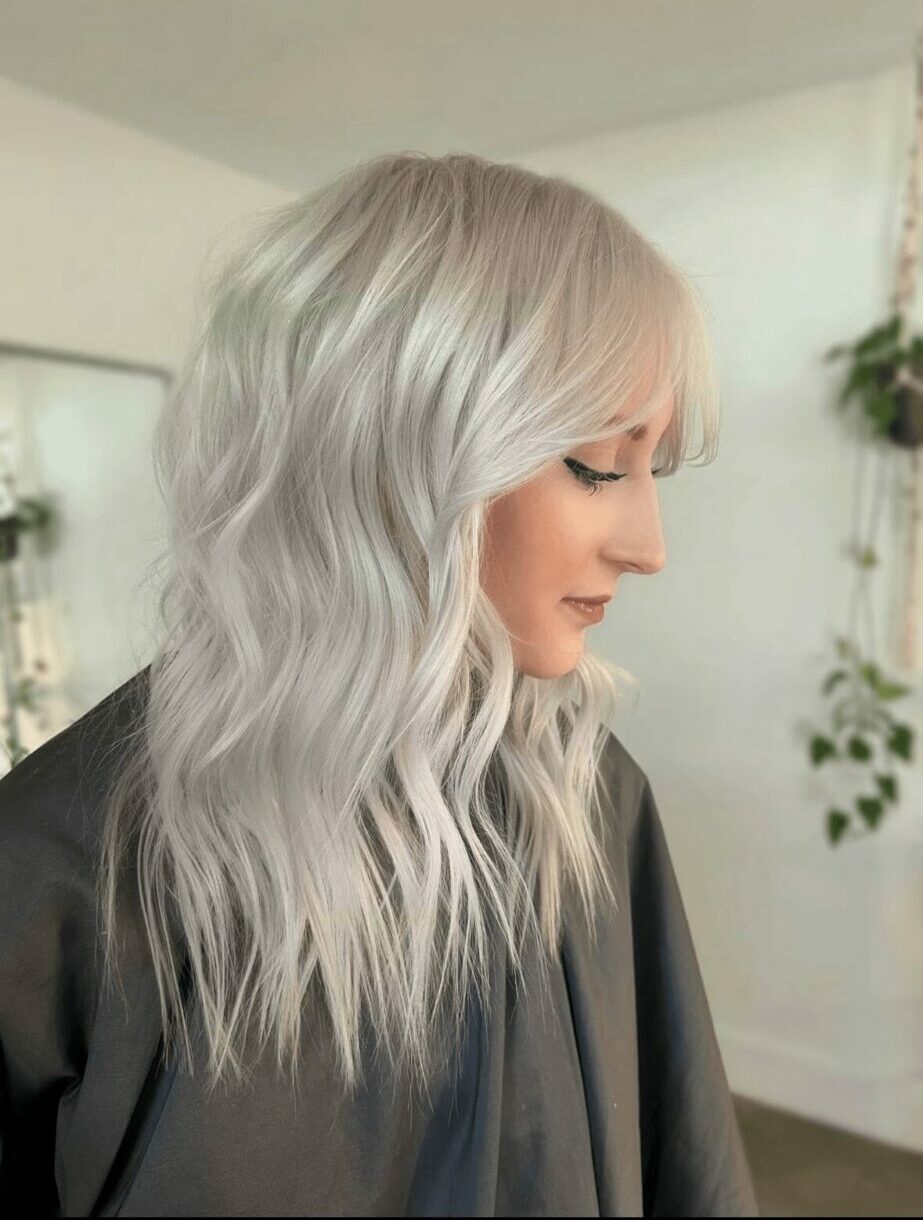 Side profile of a woman with wavy, platinum blonde hair in a bright room with plants.
