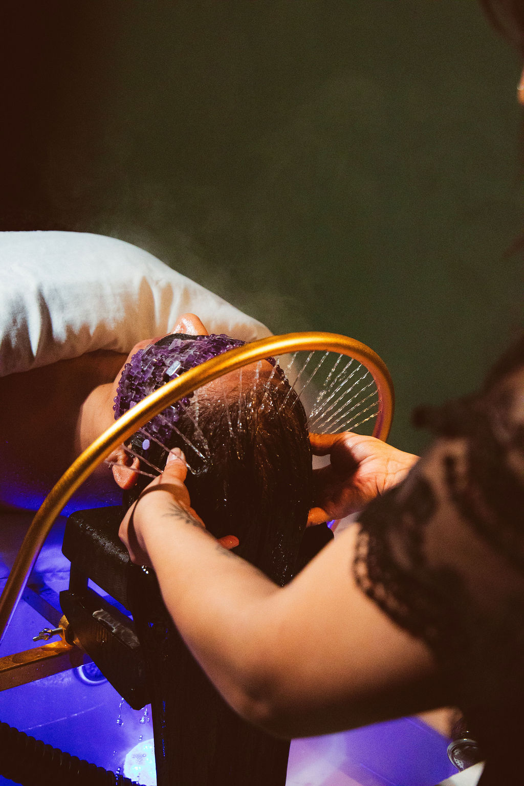 Person washing hair in a sink with a yellow handheld showerhead, wearing gloves, with a pillow supporting the head.