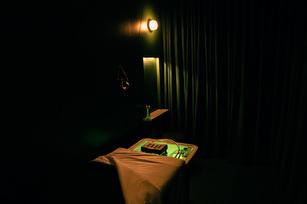 Dimly lit room with a small table, a tray, and a curtain, illuminated by a wall-mounted light.