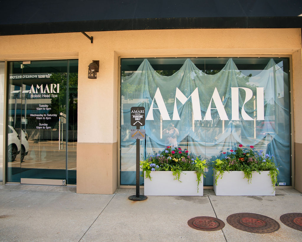 Storefront with large window displaying the word 'AMARI' and flower planters outside, beige building exterior.