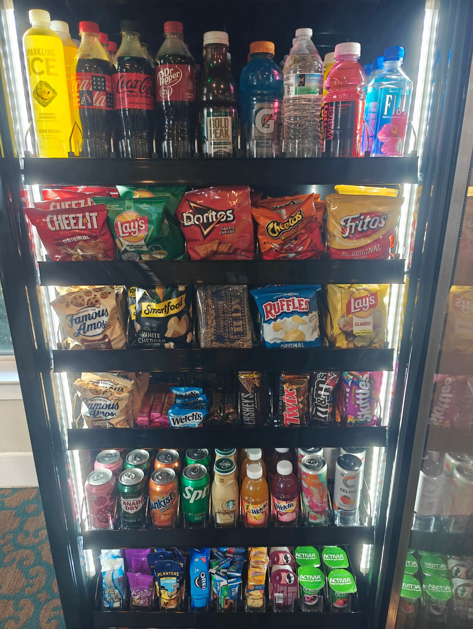 Shelf with bottled drinks, snack bags, and small snack containers arranged on four shelves.