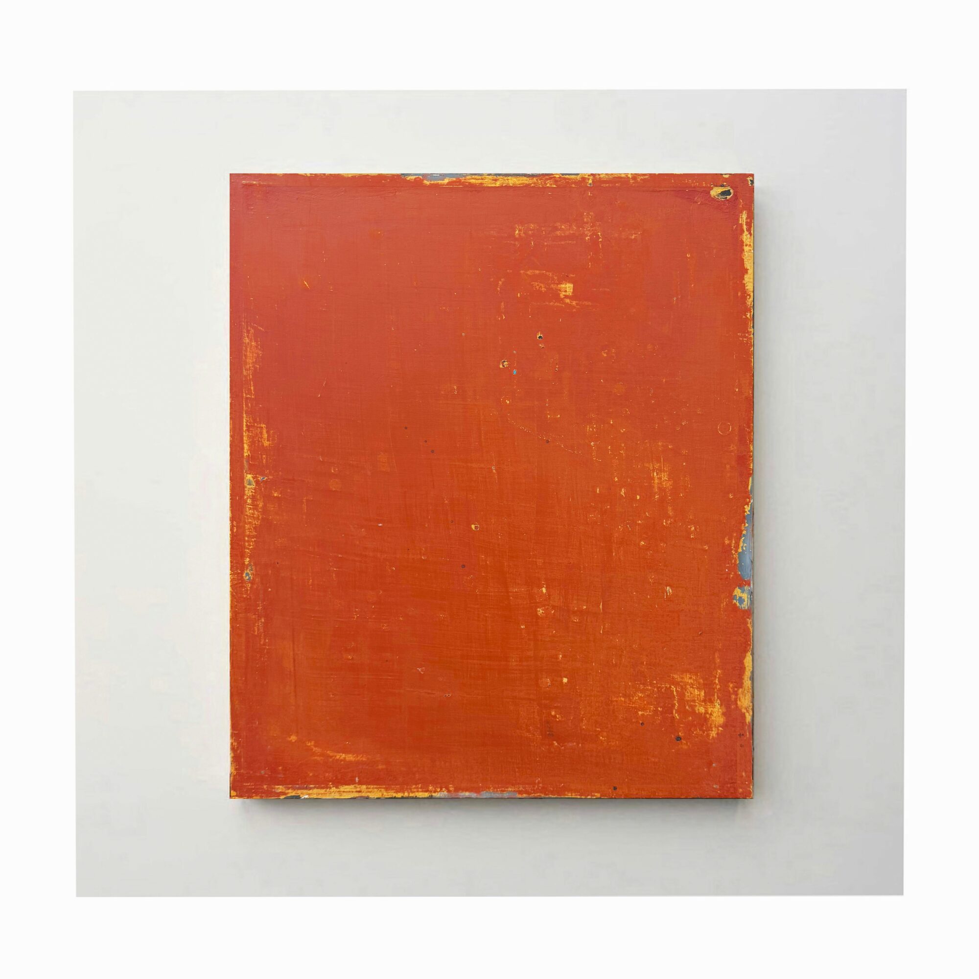 Square artwork with a red-orange textured surface and worn edges, mounted on a white wall.