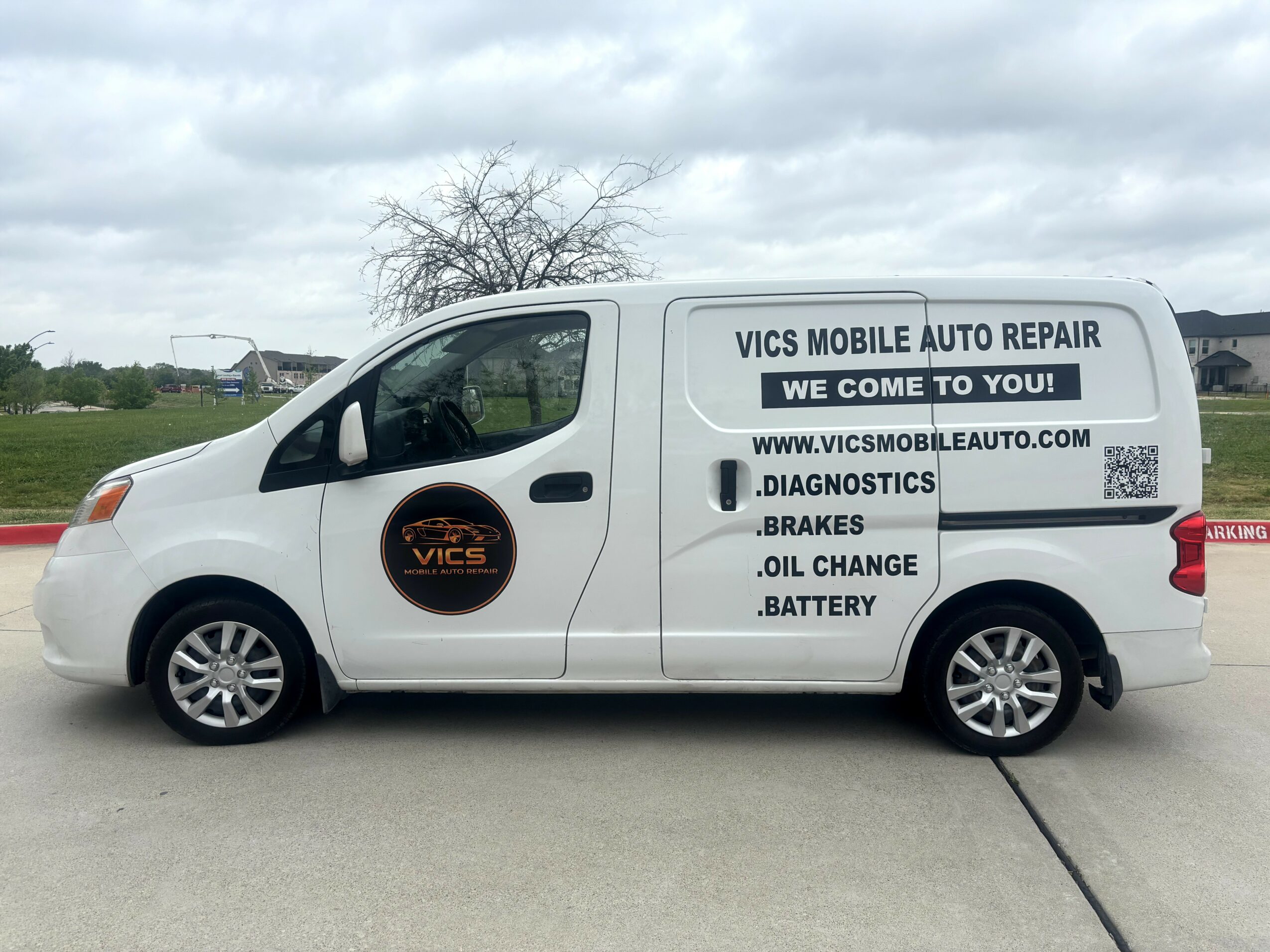 White van with black and orange logo and text advertising auto repair services, parked outdoors under cloudy sky.