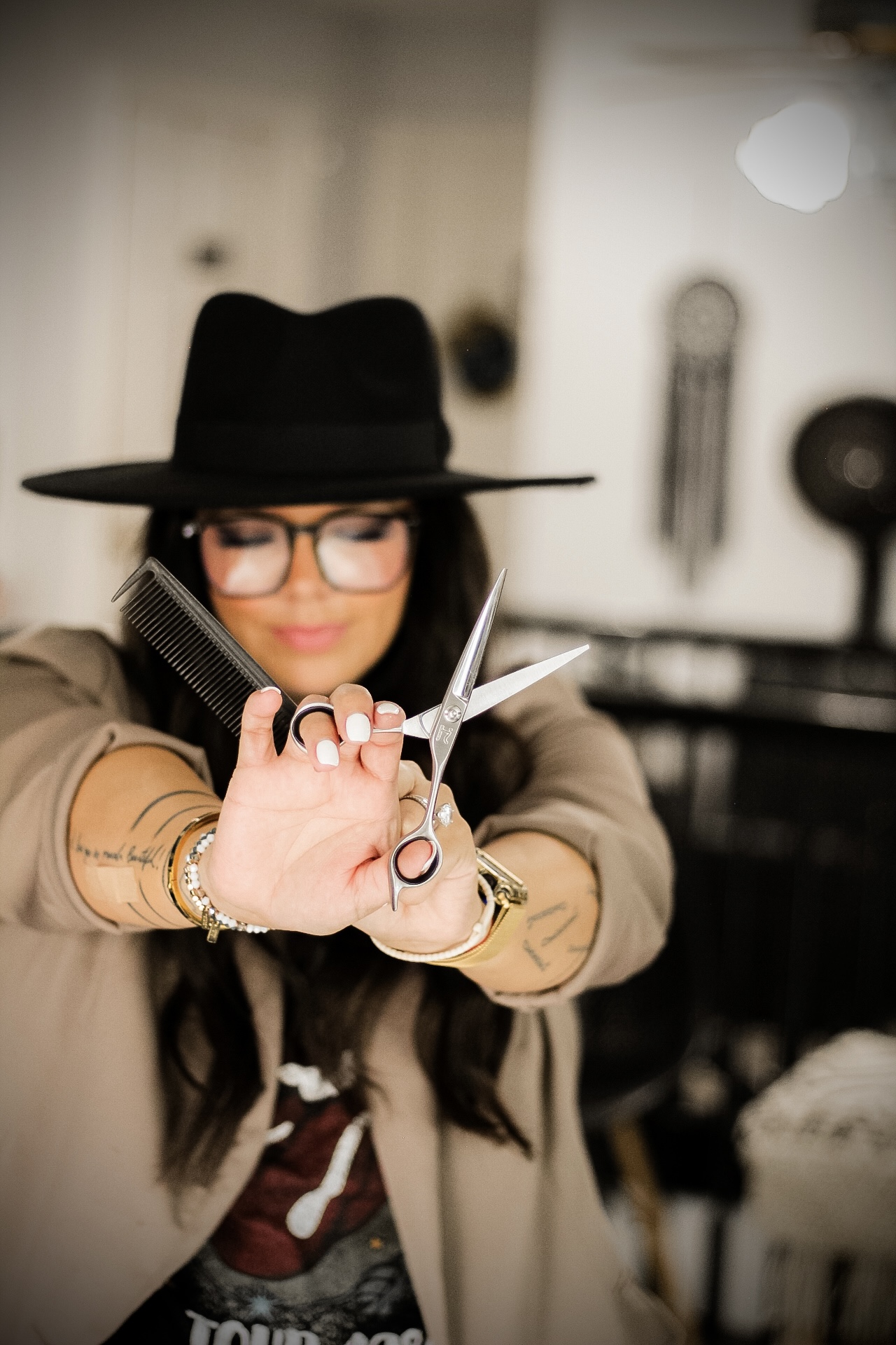Woman with glasses and a hat holds scissors, focusing on her hand and scissors, in a room with musical instruments.