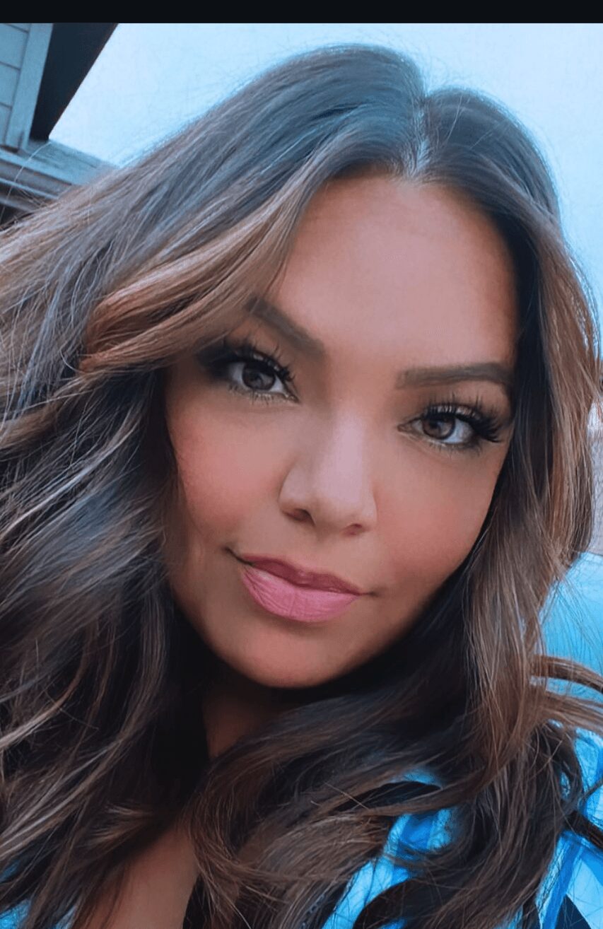 Close-up of a woman with long, wavy brown hair and makeup, smiling slightly.