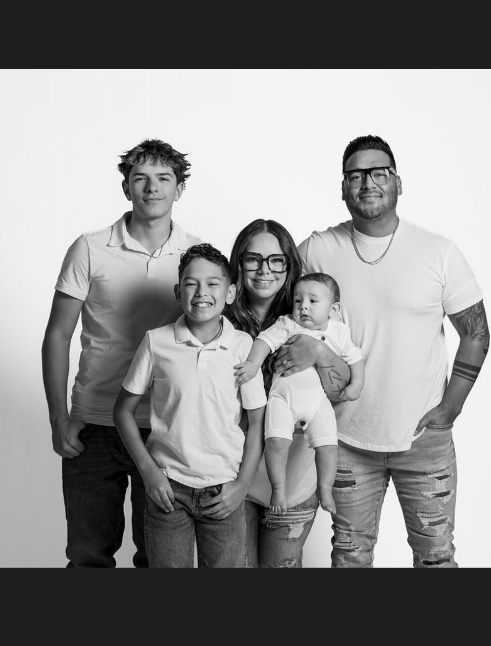 Group of five people, including children and adults, standing together in black and white, smiling, with a plain background.