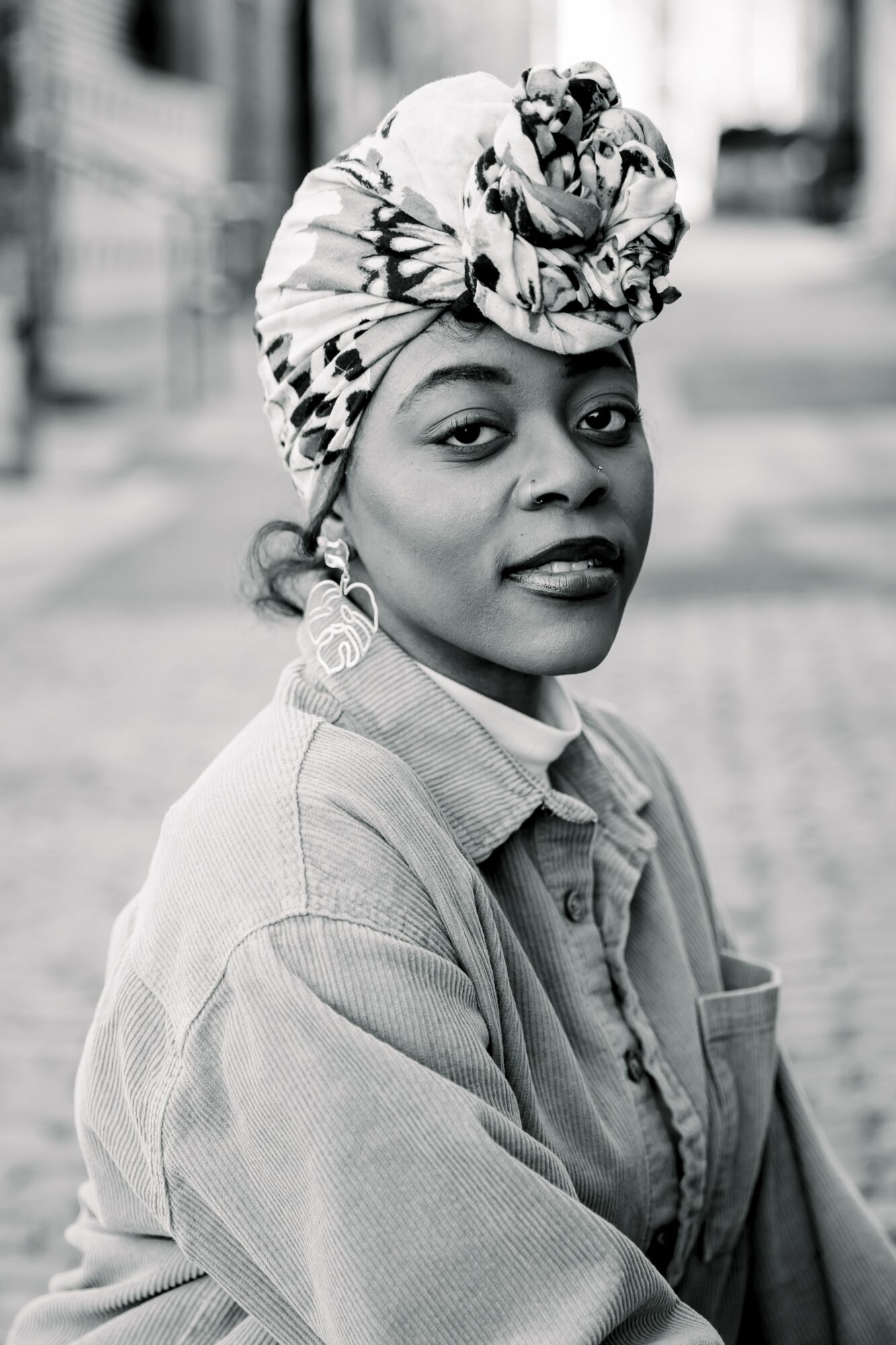 Woman wearing a headwrap and earrings, looking at the camera on a city street, in black and white.