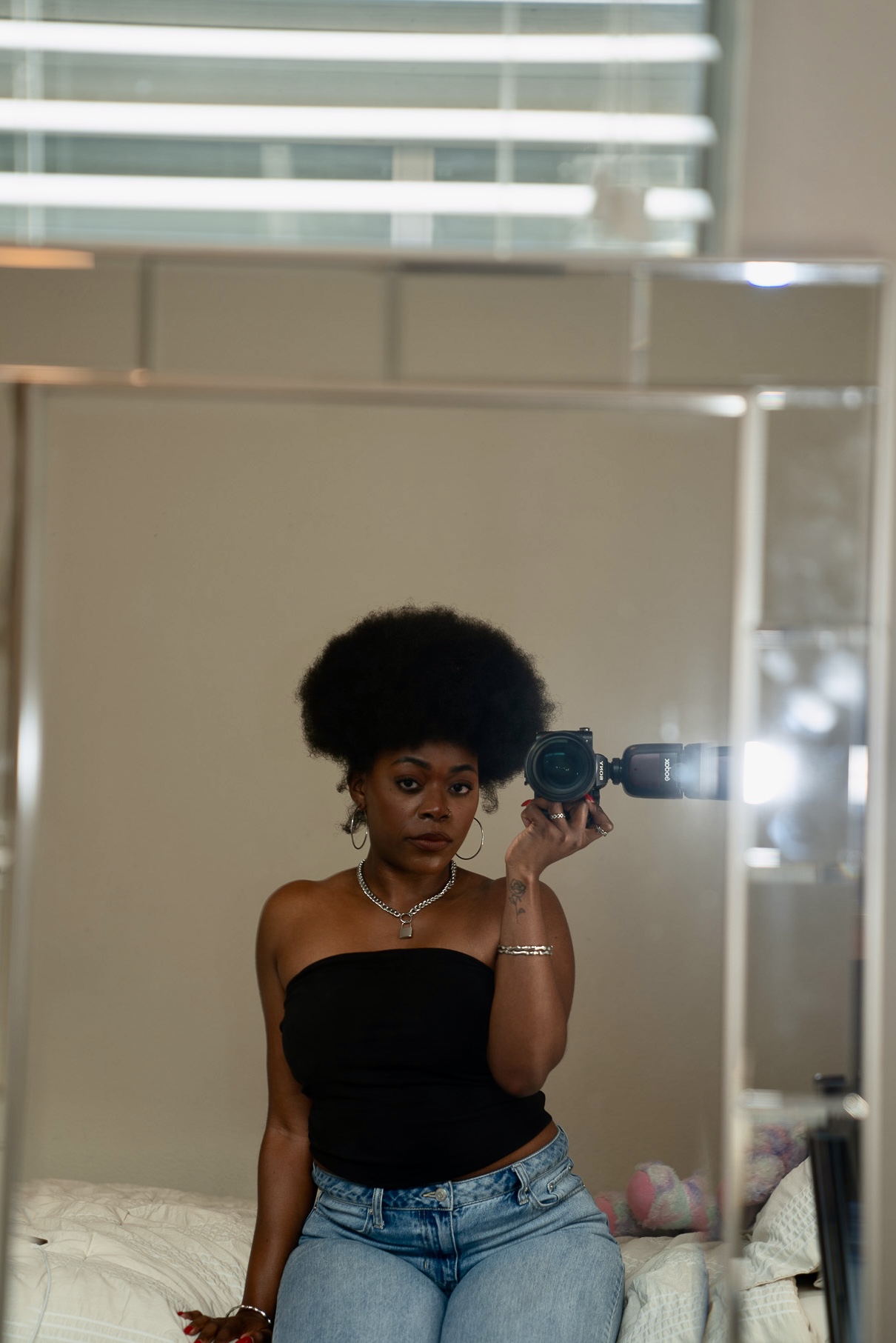 Woman with curly hair taking a mirror selfie in a room, wearing a black strapless top and jeans.